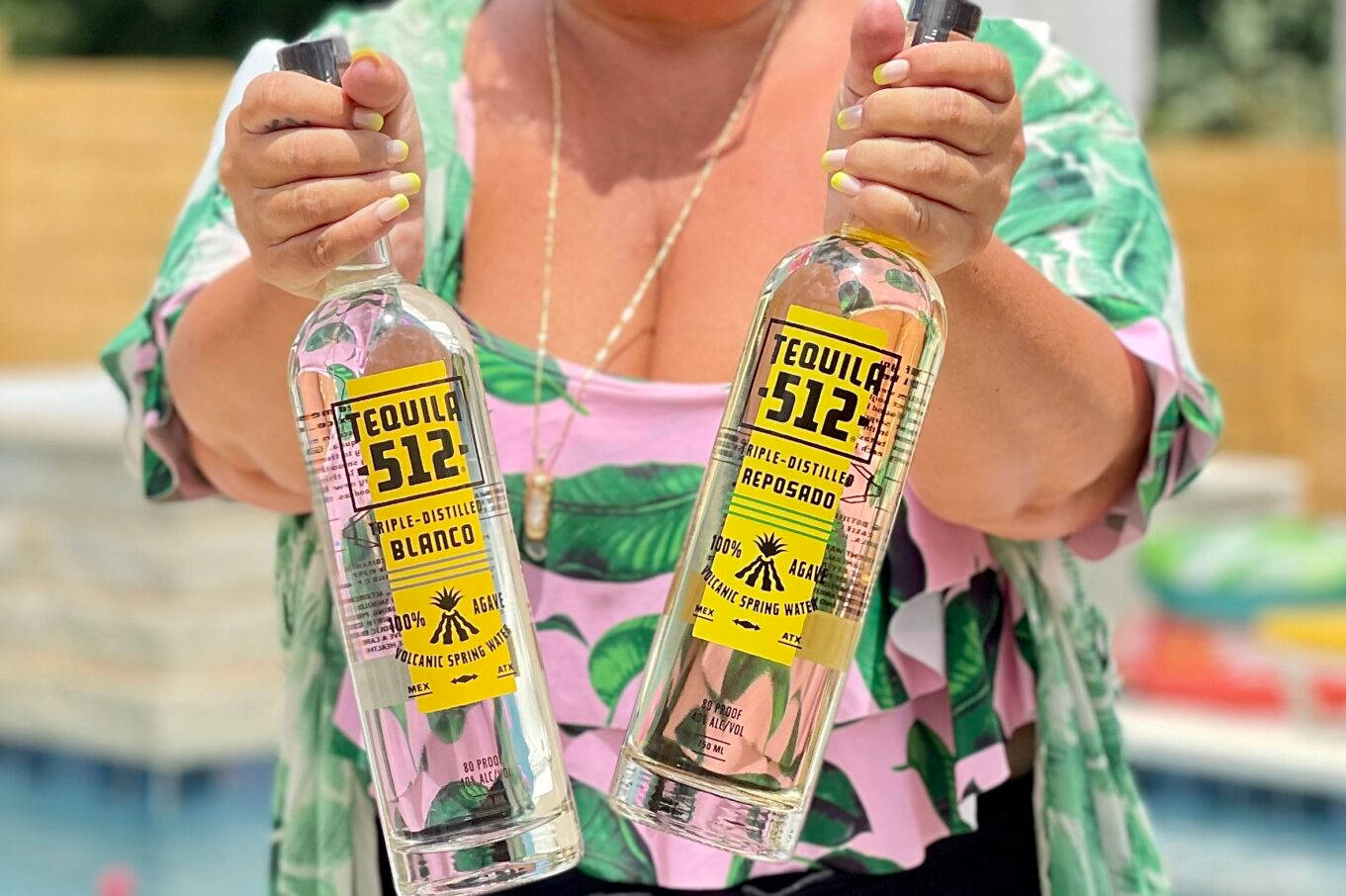drinks 桌布 壁紙 — 一位身穿熱帶印花上衣的女性在明媚陽光下，在泳池邊拿著兩瓶透明的Tequila 512。
