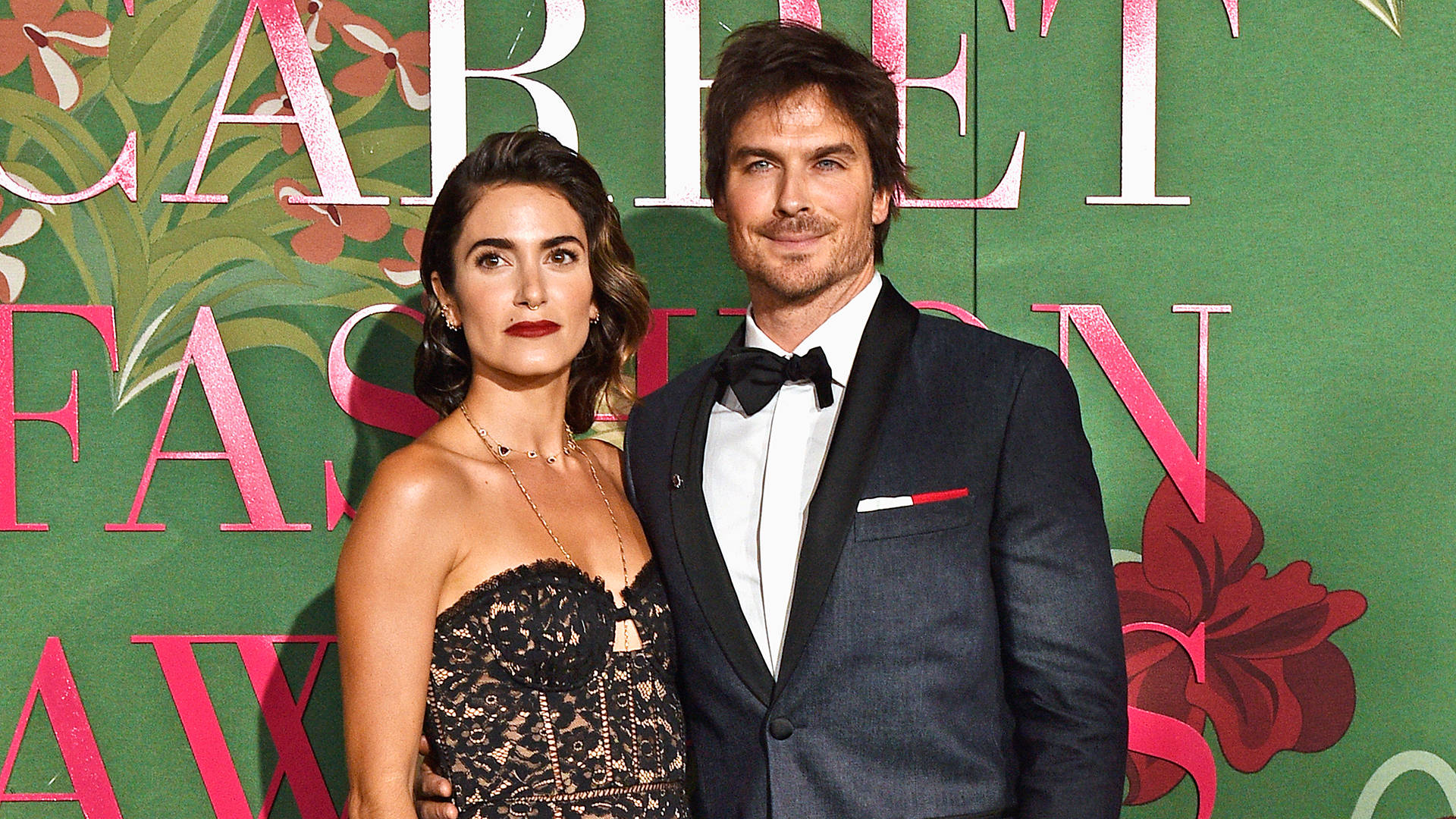 電影動圖 桌布 壁紙 — 一位身穿燕尾服的男士和一位身穿黑色蕾絲裙的女士在綠色花卉背景前的時尚頒獎活動中一起擺姿勢。