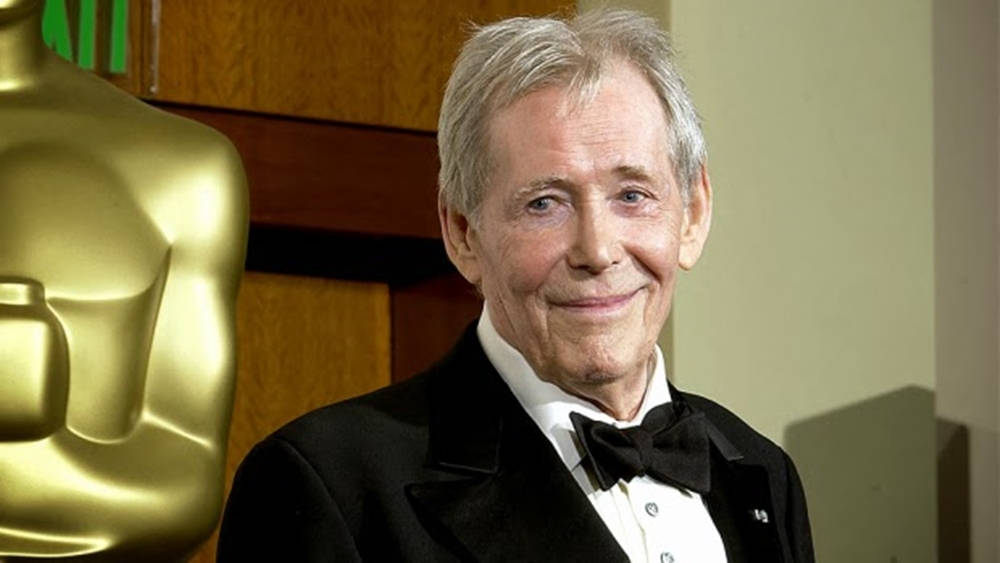 actor 桌布 壁紙 — 一位身穿燕尾服的長者在溫暖的室內燈光下，微笑地站在金色奧斯卡獎座旁。