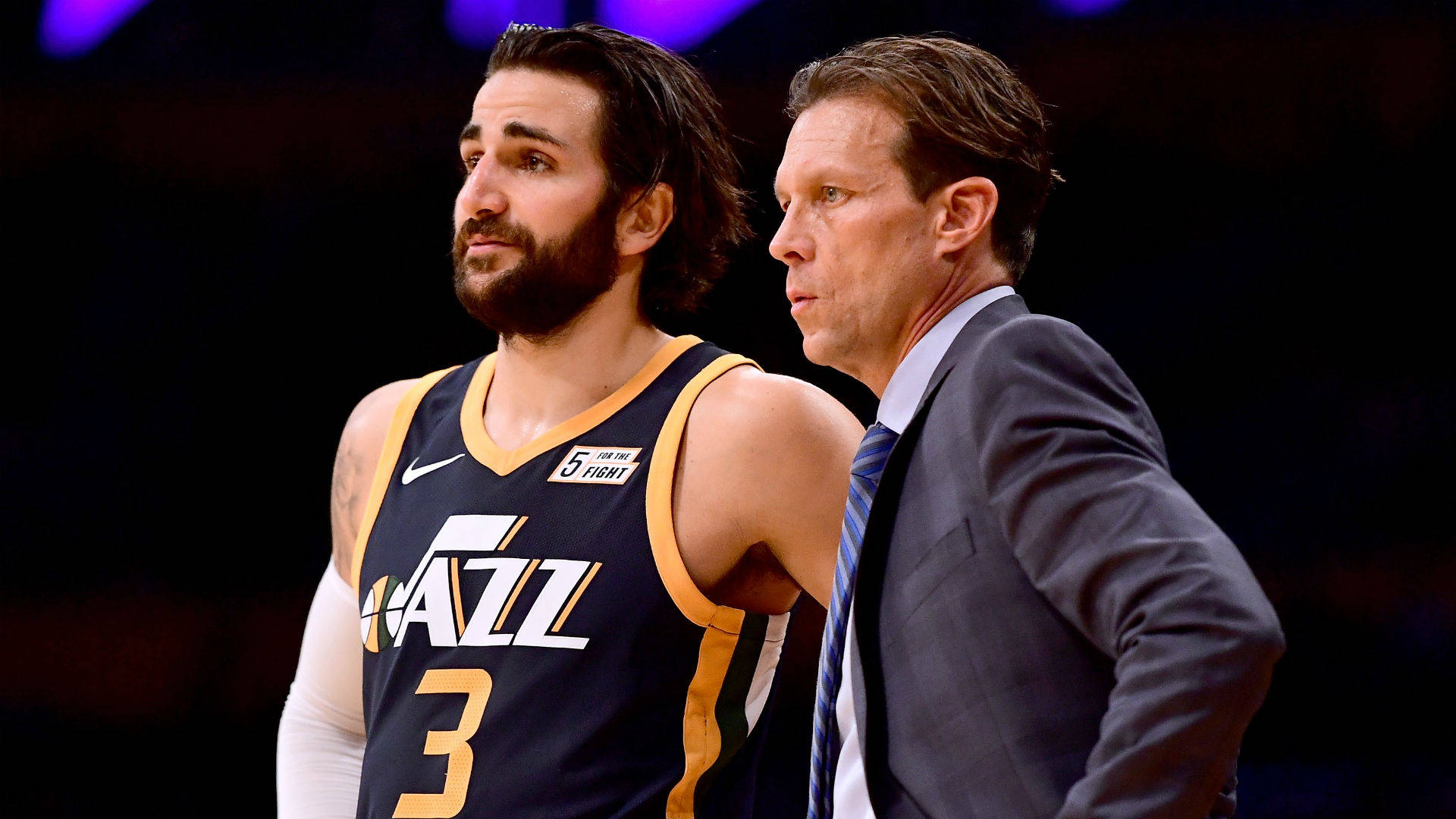 Ricky Rubio 桌布 壁紙 — 一位身穿爵士隊球衣的籃球運動員在比賽期間，於場館燈光下站在教練旁邊。
