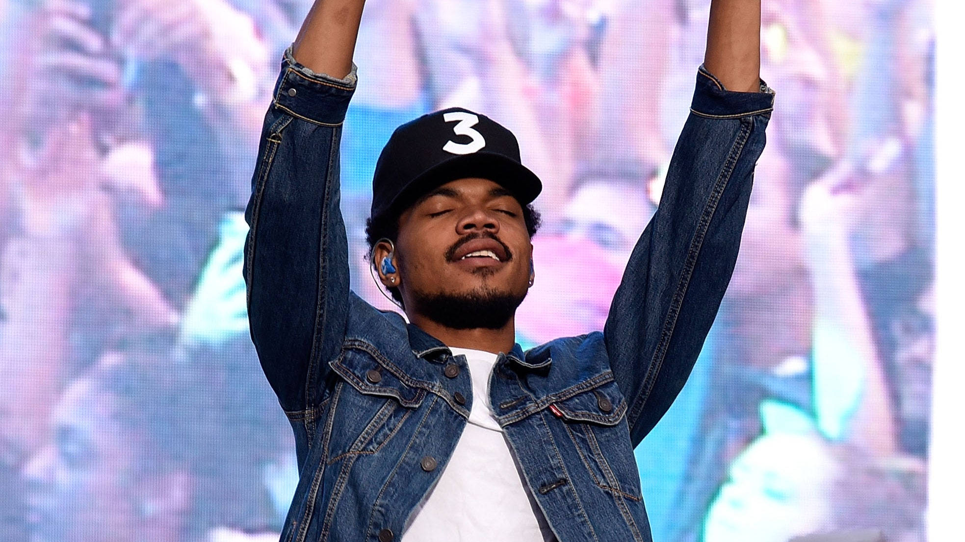 chance 桌布 壁紙 — 一位身穿牛仔外套和帽子的男性表演者在舞台上，在閃耀的人群前勝利地舉起雙臂。