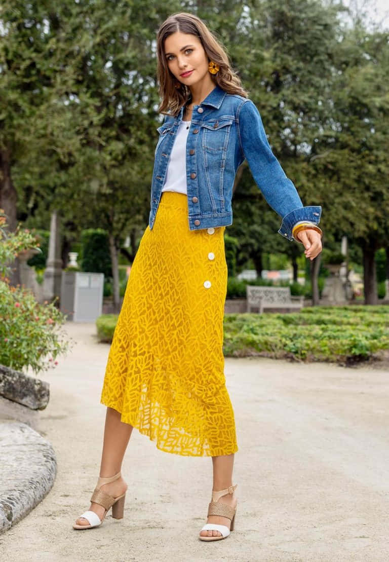 Spring Fashion 桌布 壁紙 — 一位身穿牛仔外套和鮮黃色蕾絲裙的女性自信地走過鬱鬱蔥蔥的綠色公園。
