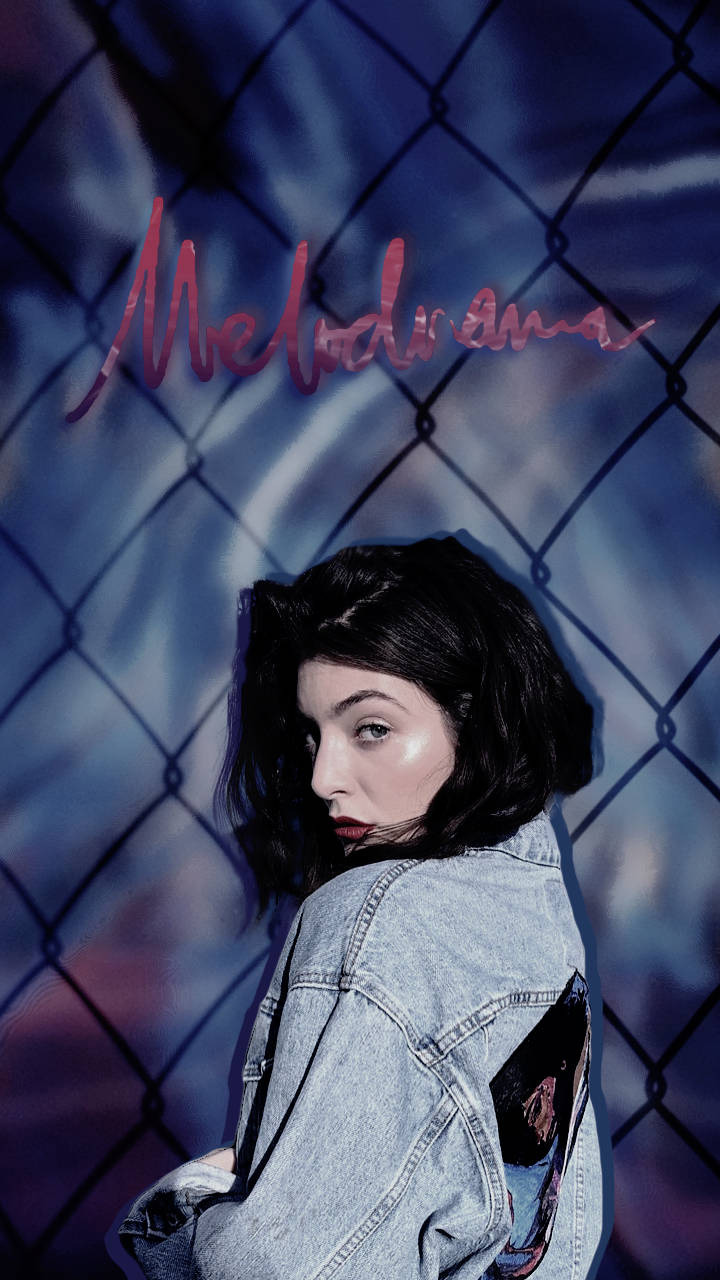 Lorde 桌布 壁紙 — 一位身穿牛仔外套的年輕女性在鐵絲網圍欄後方回頭凝視，背景是憂鬱的藍色，並有粉紅色字體的「Melodrama」字樣。