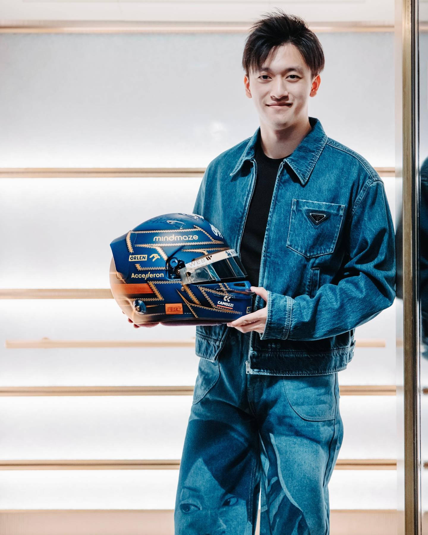 Men 桌布 壁紙 — 一位身穿牛仔布的年輕男子，在現代條紋背景前手持藍金色賽車頭盔。