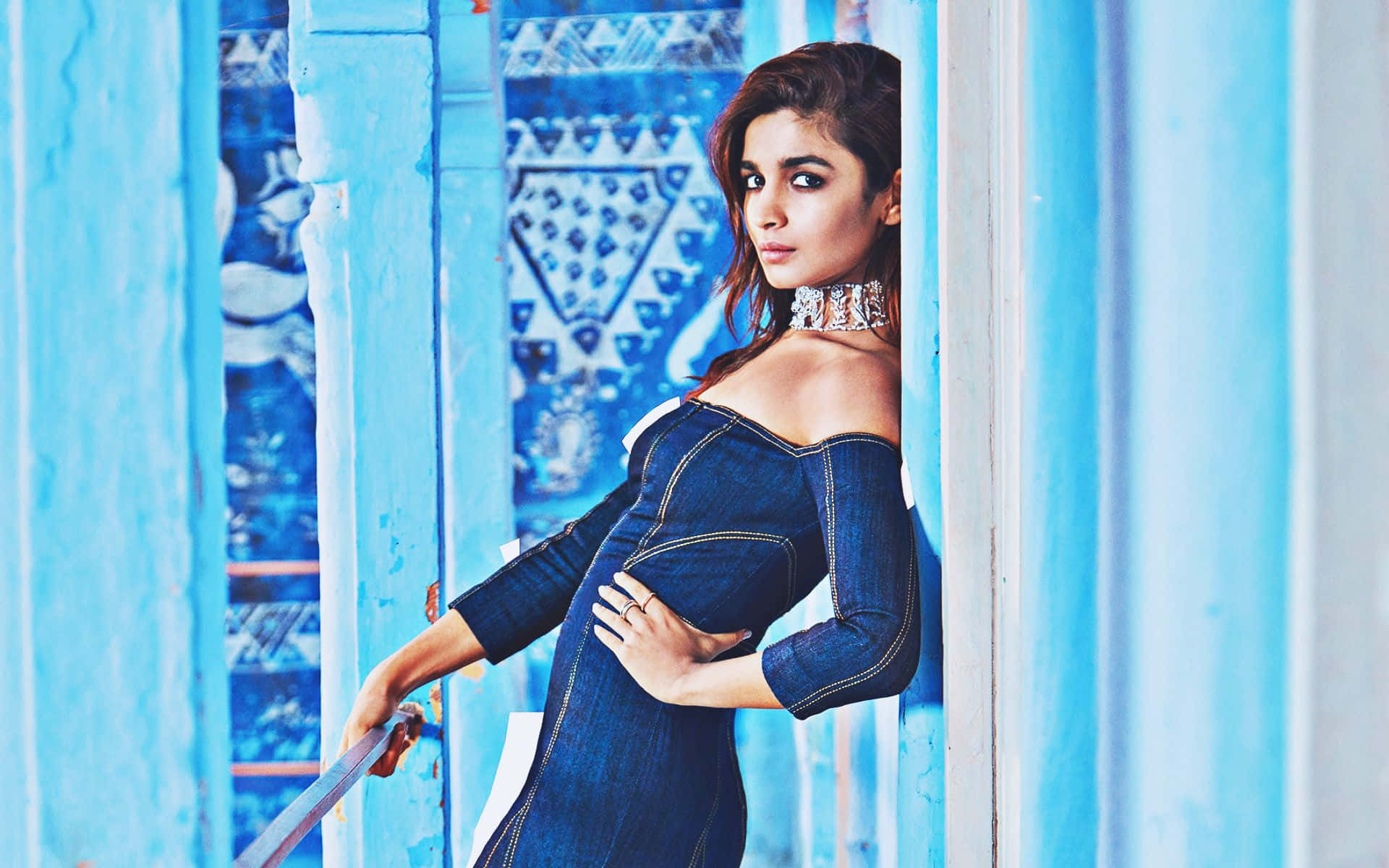 Alia Bhatt 桌布 壁紙 — 一位身穿牛仔裙的女性靠在她身後帶有幾何圖案的鮮豔藍色木板上。