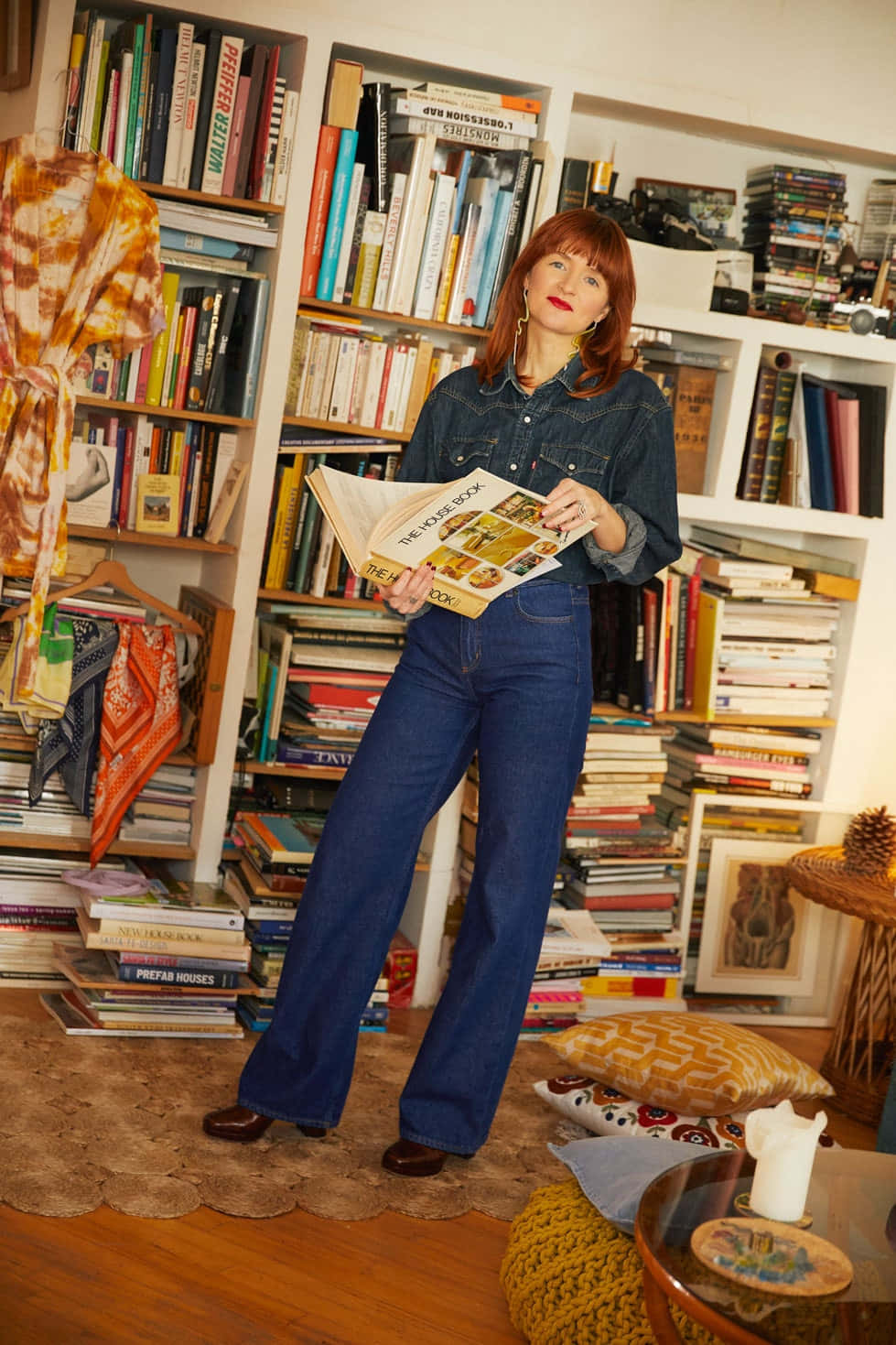 Bookshelf 桌布 壁紙 — 一位身穿牛仔褲和牛仔襯衫的女性站在一個舒適、充滿書籍的房間裡，手持一本打開的書。