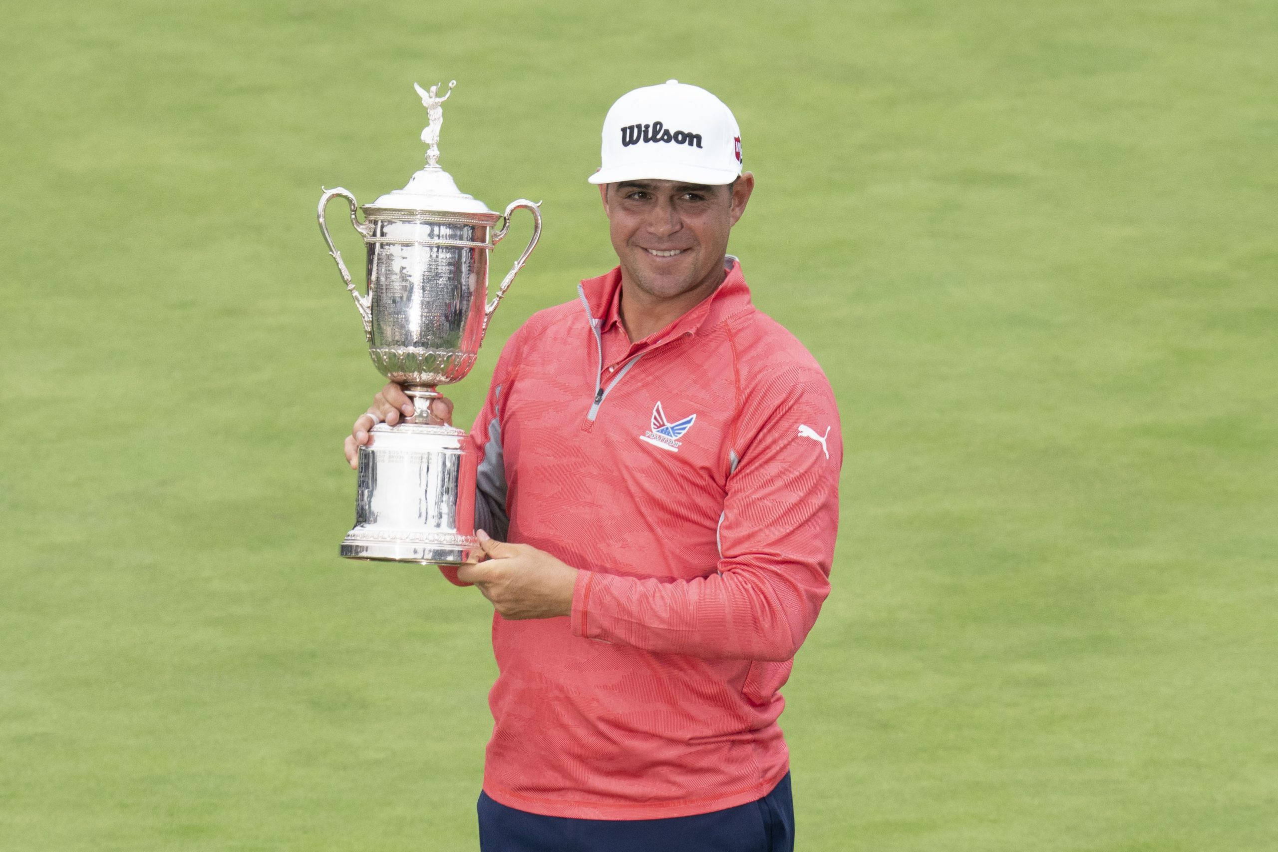 Trophy 桌布 壁紙 — 一位身穿珊瑚色襯衫、面帶微笑的高爾夫球手，在翠綠的高爾夫球場上自豪地高舉一個大型銀色獎盃。