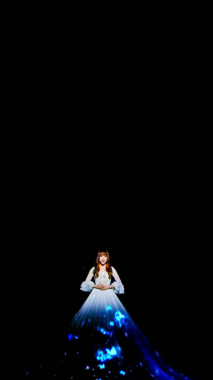 K-pop 桌布 壁紙 — 一位身穿發光藍白長裙的女性獨自站在漆黑背景前，伴隨著閃爍的光效。