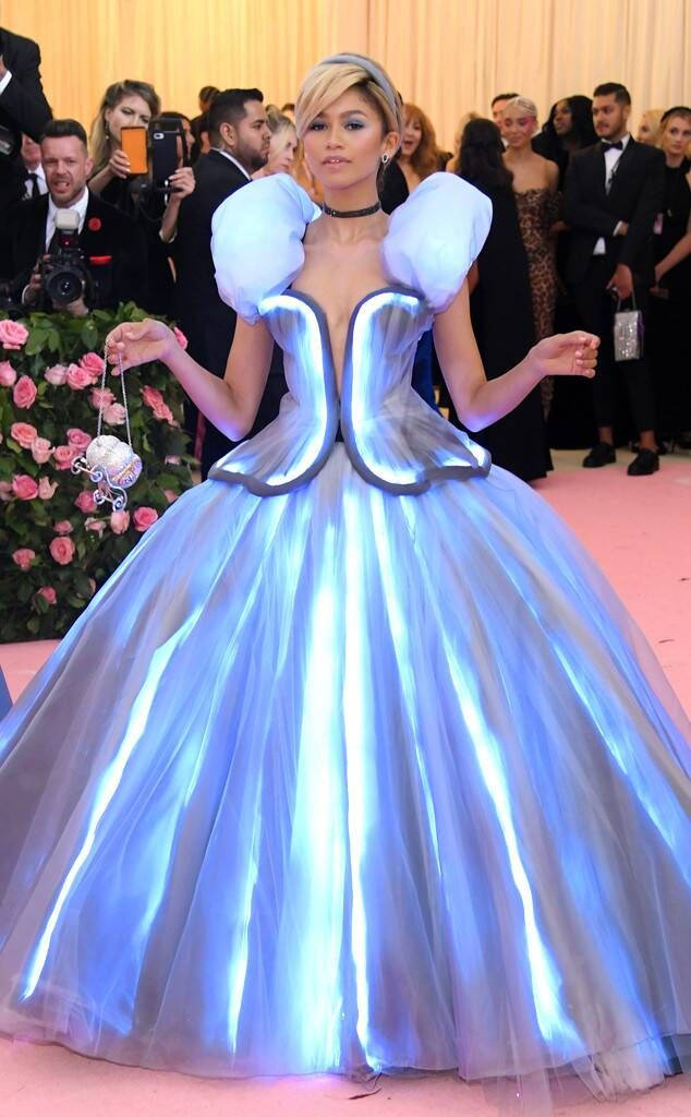 Zendaya 桌布 壁紙 — 一位身穿發光藍色未來主義連衣裙、帶有蓬鬆袖子的女士在粉紅色地毯上擺姿勢，參加一場華麗的活動。