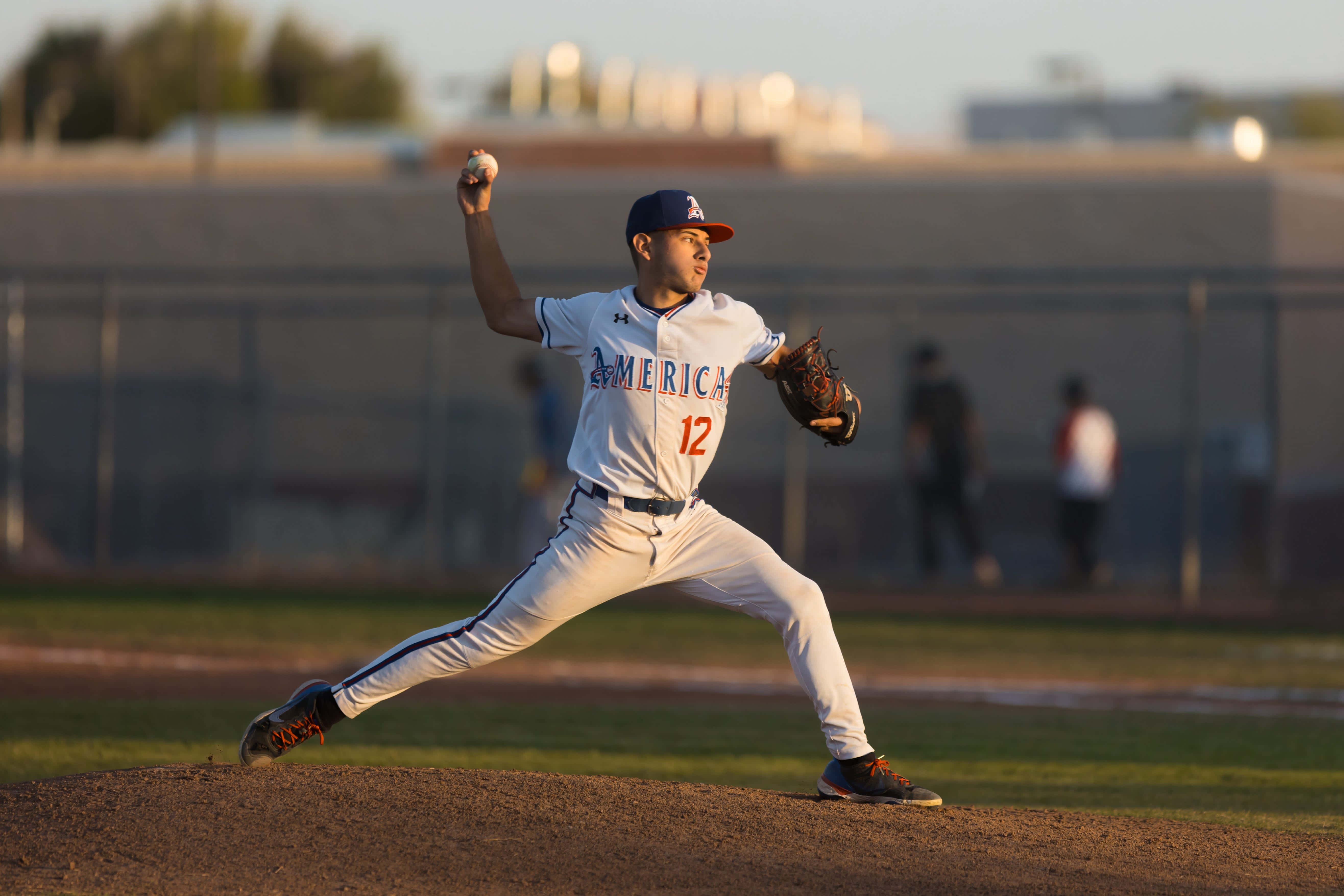 College Baseball 桌布 壁紙 — 一位身穿白色12號球衣的棒球投手，在金色夕陽下於投手丘上準備投球。