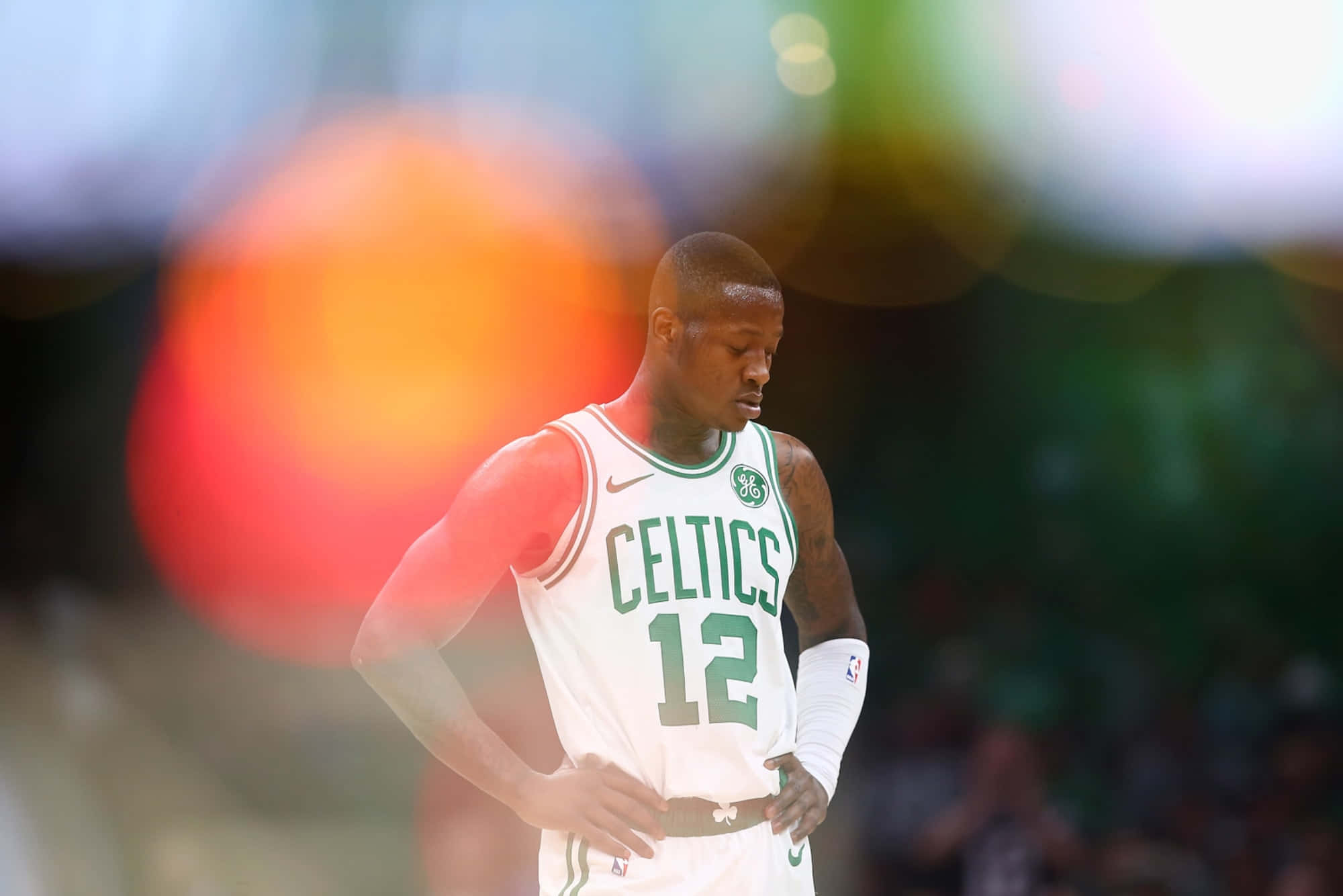 NBA 桌布 壁紙 — 一位身穿白色12號球衣的波士頓塞爾提克籃球運動員，在比賽中雙手叉腰低頭站立，背景是模糊的體育場燈光。