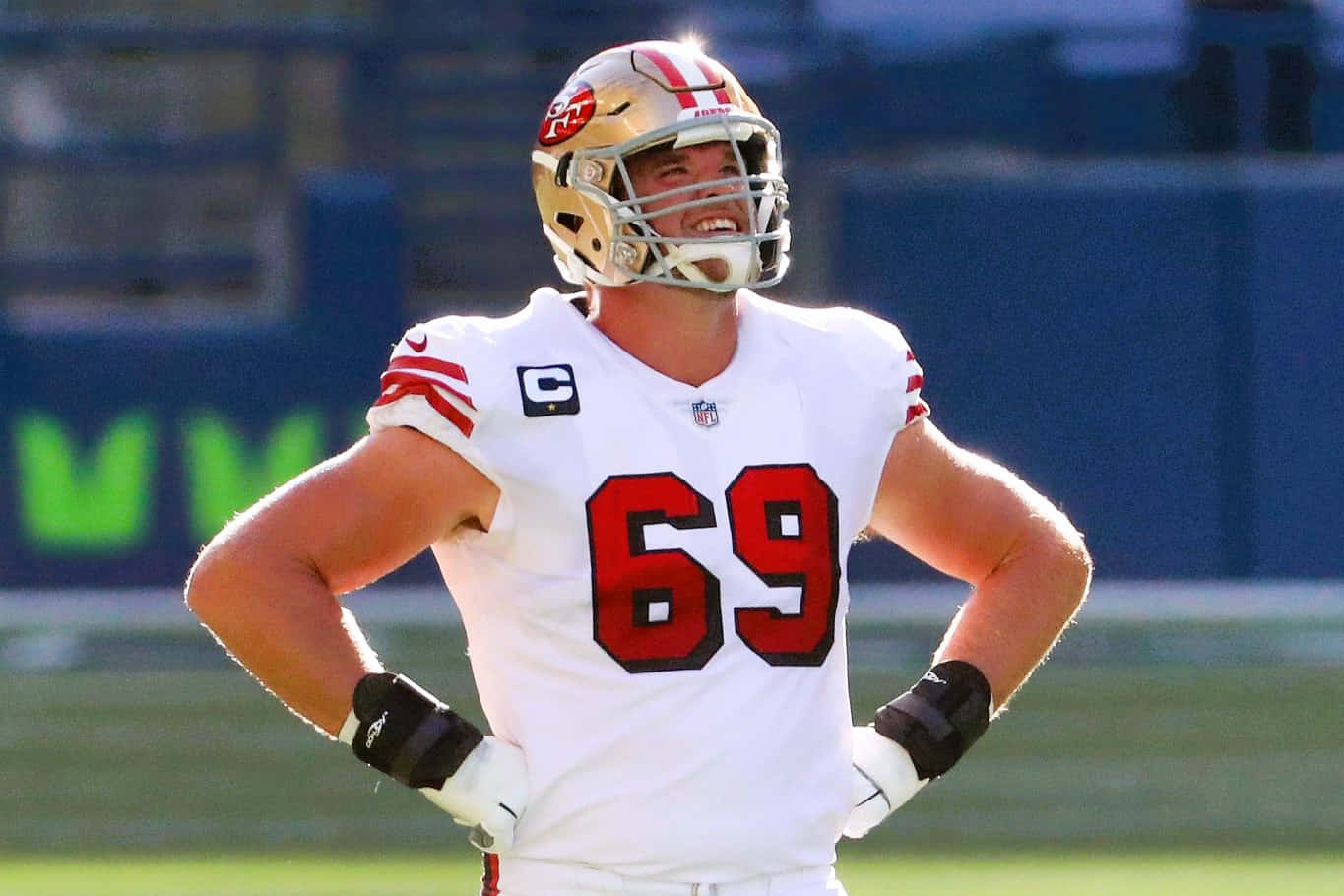 Mike Mcglinchey 桌布 壁紙 — 一位身穿白色69號球衣的舊金山49人美式足球員，自信地站在陽光明媚的球場上，雙手叉腰。