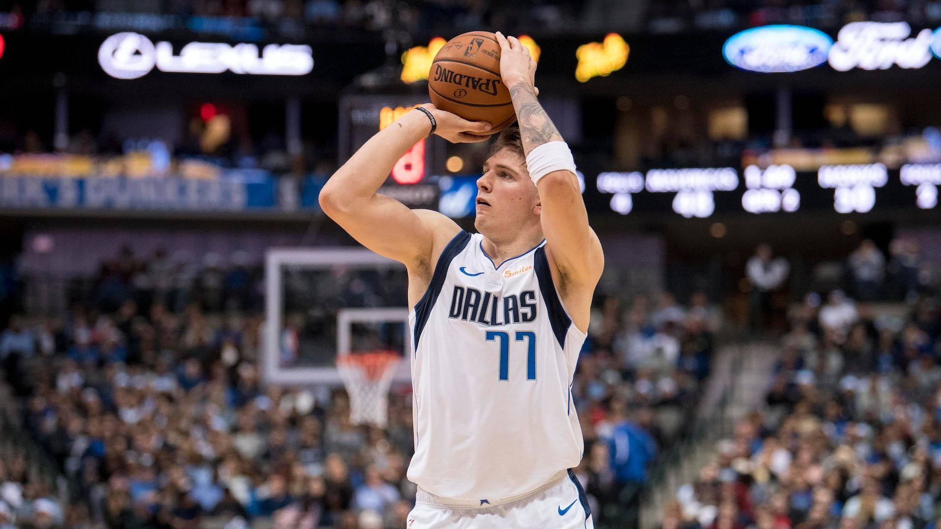 Luka 桌布 壁紙 — 一位身穿白色77號球衣的達拉斯獨行俠籃球運動員，在明亮的場館燈光下準備投籃，背景是模糊的人群。