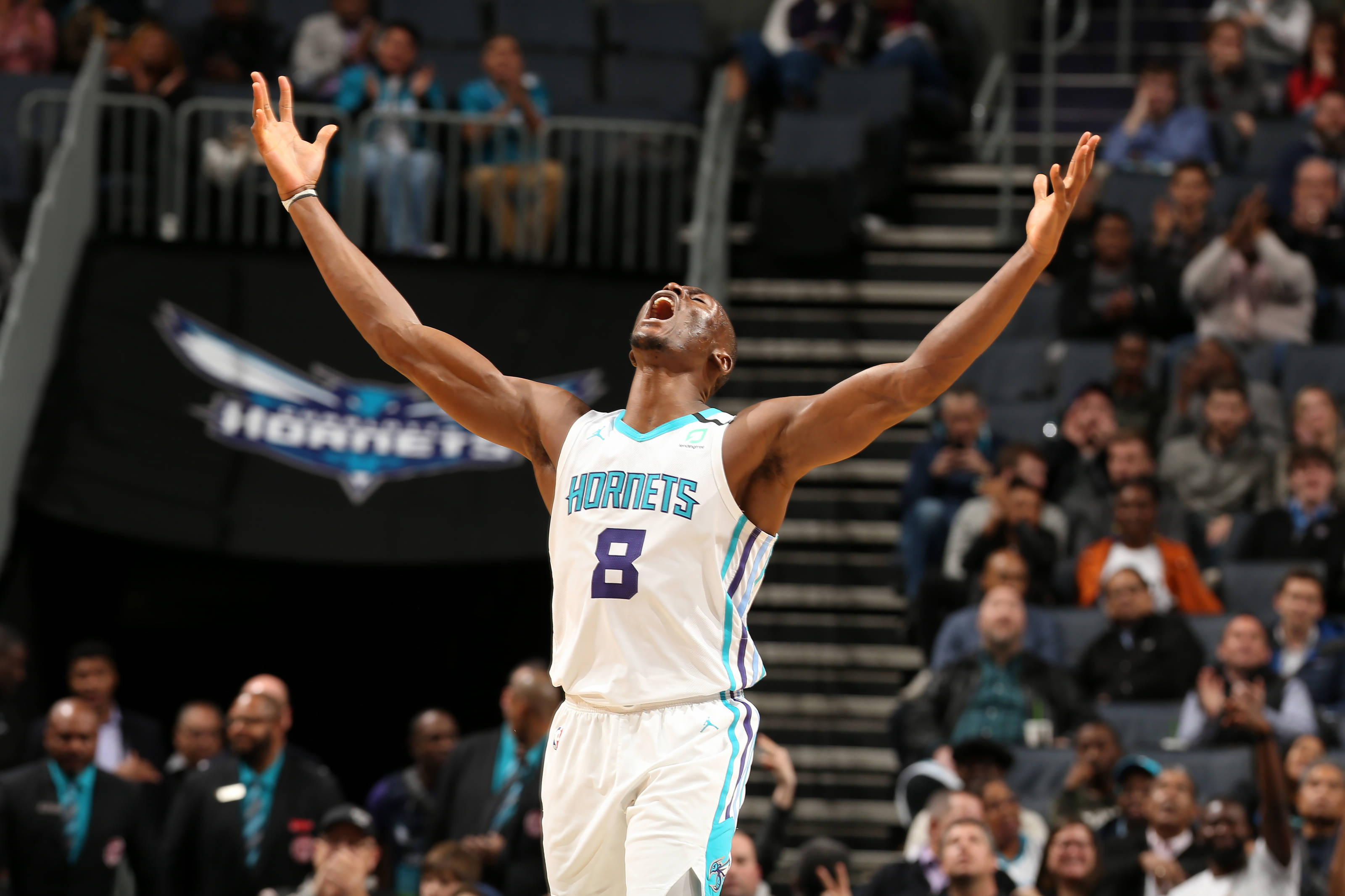 Hornets 桌布 壁紙 — 一位身穿白色8號球衣的夏洛特黃蜂隊籃球運動員在座無虛席的球場上高舉雙臂慶祝勝利。