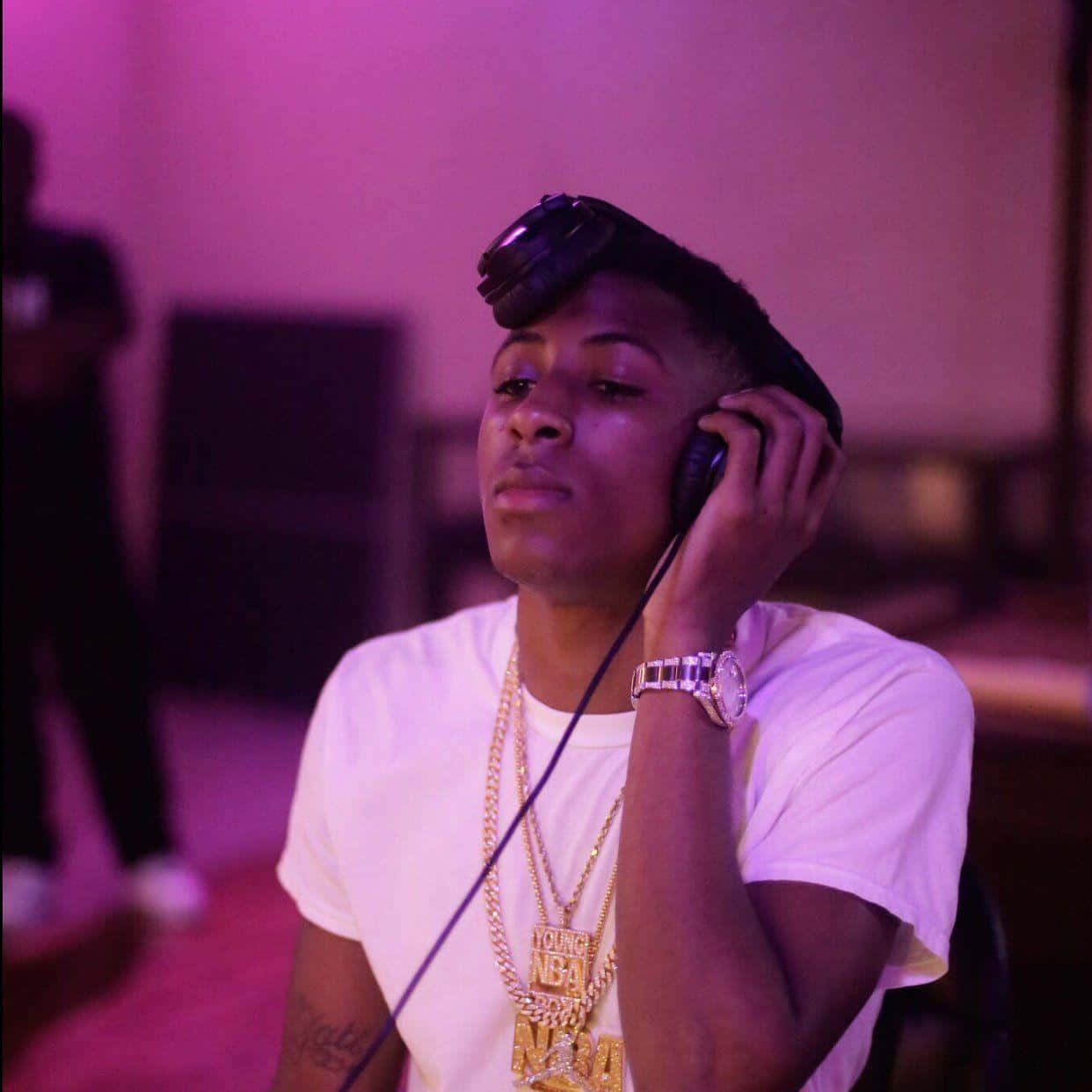 Youngboy 桌布 壁紙 — 一位身穿白色T恤和金色鏈條的年輕男子在紫色環境燈光下透過耳機專注地聆聽。