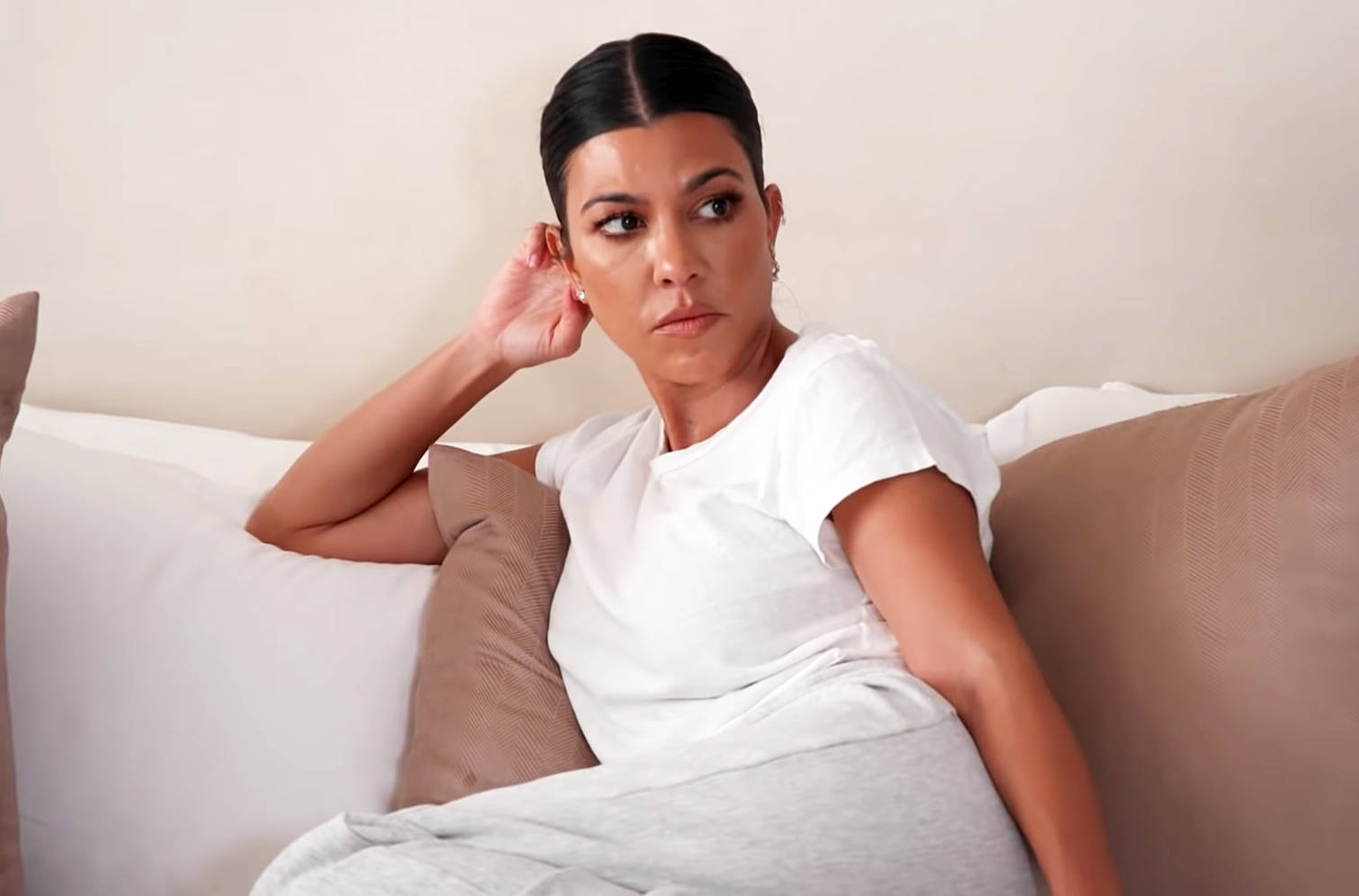 Kourtney 桌布 壁紙 — 一位身穿白色T恤的女人坐在米色沙發上，用手掩住耳朵，表情充滿懷疑。