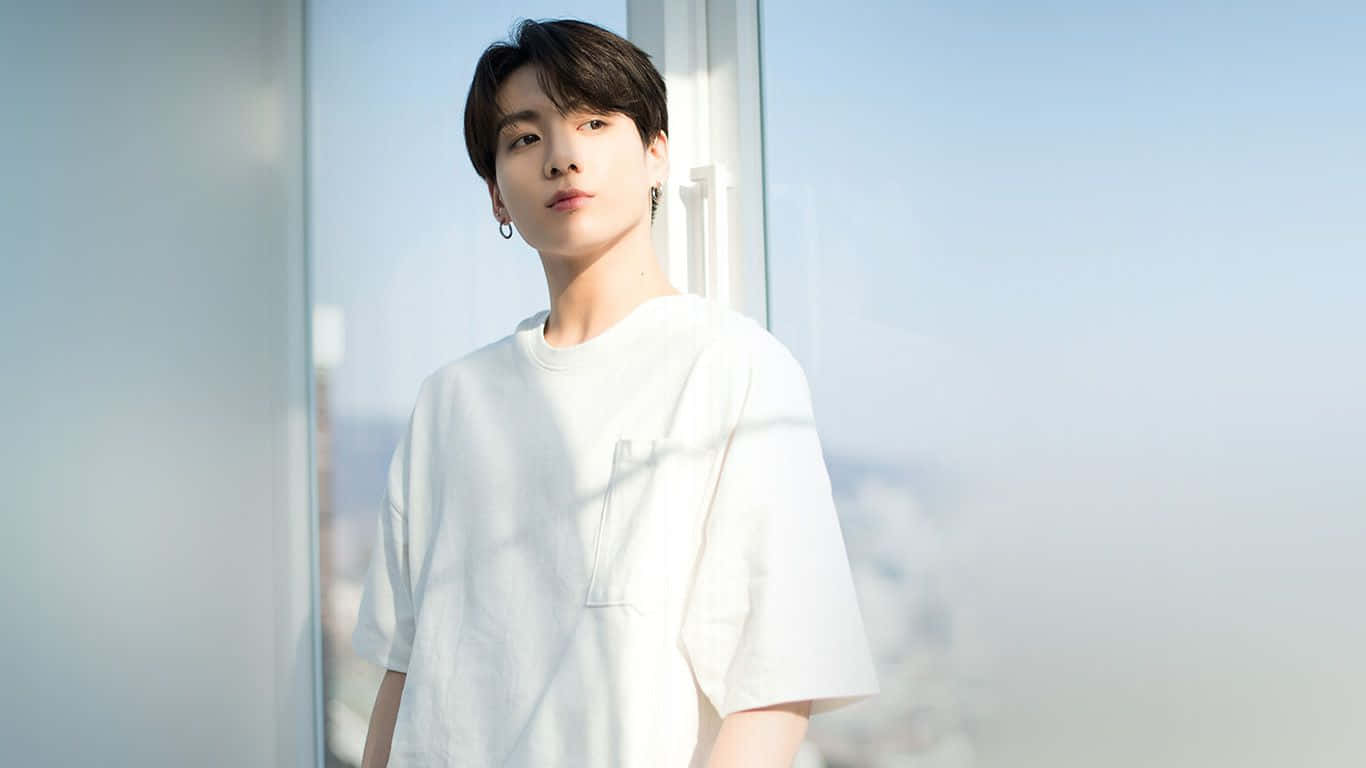 Bts Mac 桌布 壁紙 — 一位身穿白色T恤的年輕男子站在明亮的窗邊，身後的城市景觀模糊不清。