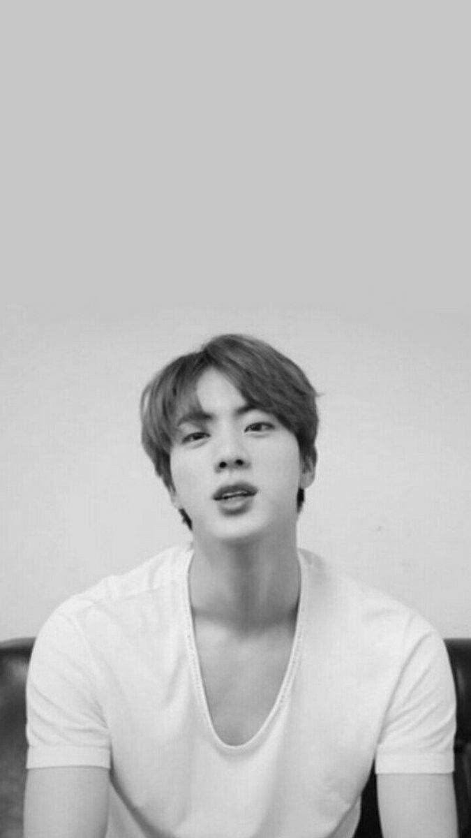 Jin 桌布 壁紙 — 一位身穿白色V領襯衫的年輕男子，在純色淺色背景下，帶著柔和的表情向上凝視。