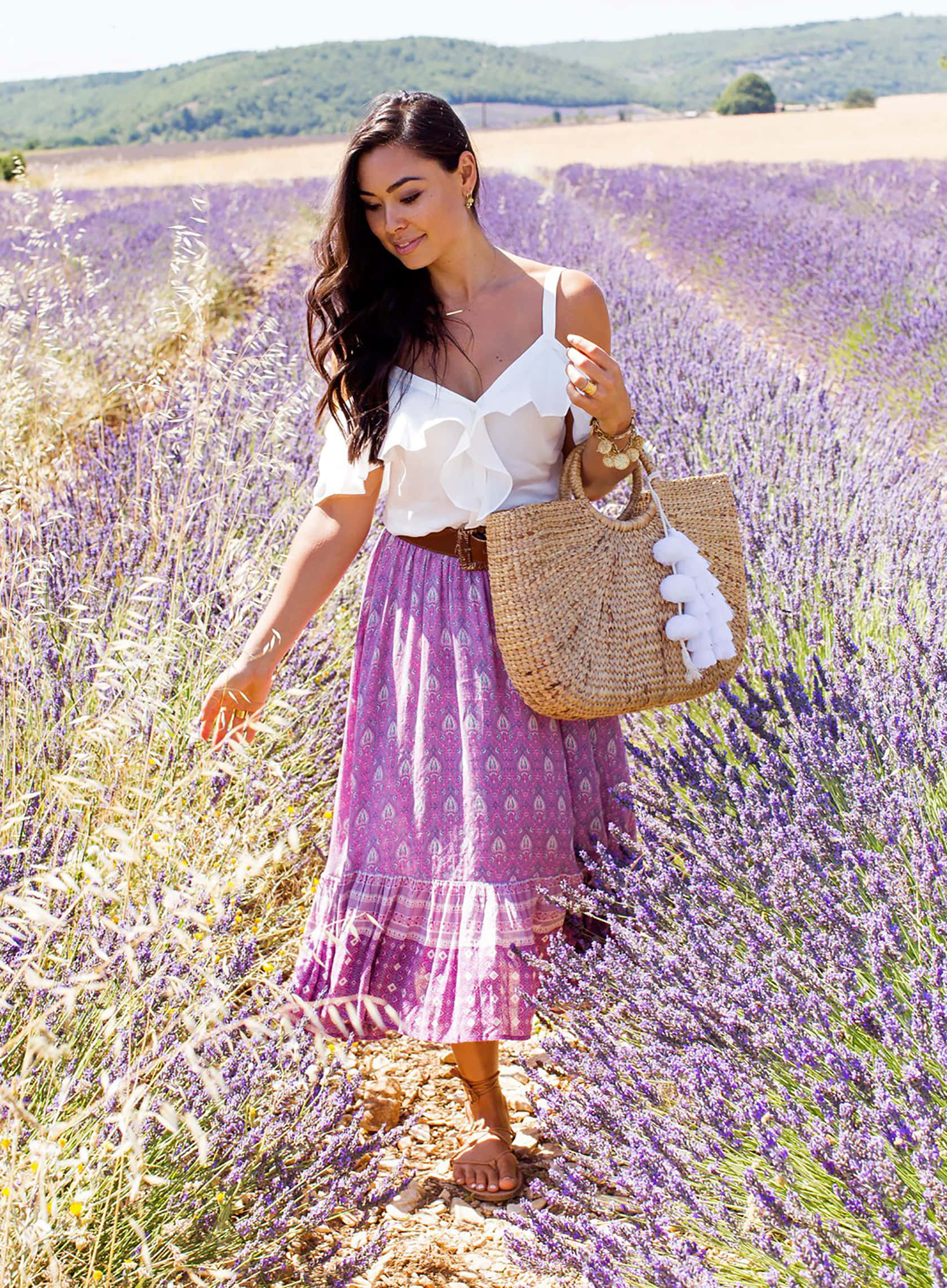 Spring Fashion 桌布 壁紙 — 一位身穿白色上衣和紫色圖案裙子的女士，手持編織手提袋，走過陽光普照的薰衣草田。