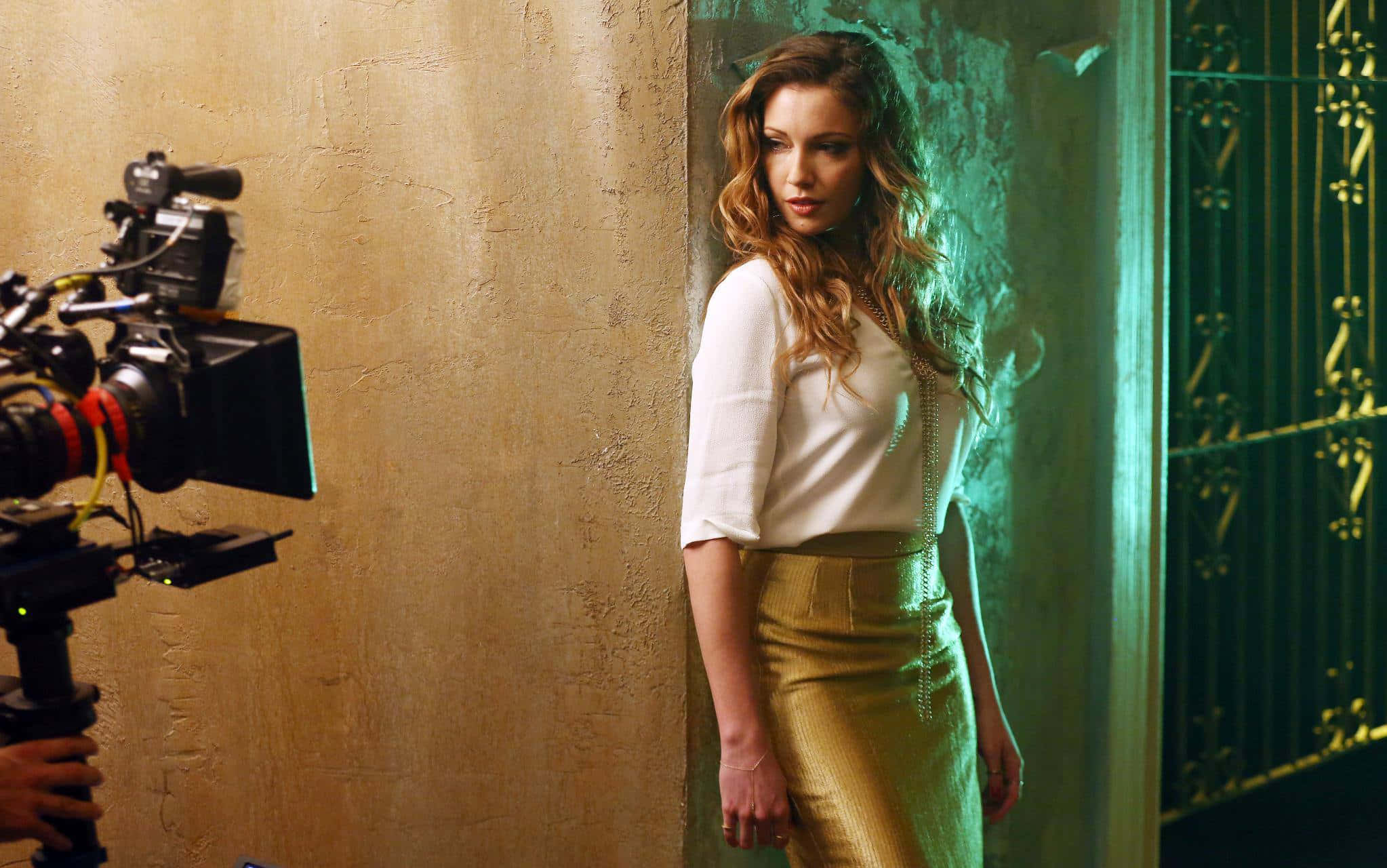 katie cassidy 桌布 壁紙 — 一位身穿白色上衣和金色裙子的女士靠在一面有紋理的牆上，攝製組在一個氣氛濃郁的綠色燈光工作室中拍攝她。