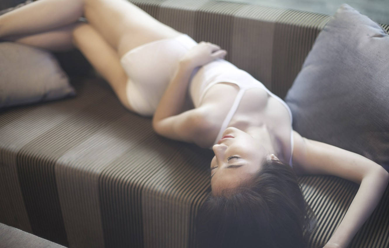 Sexy 桌布 壁紙 — 一位身穿白色內衣的女性在光線昏暗的房間裡，放鬆地躺在帶有柔軟枕頭的條紋沙發上。