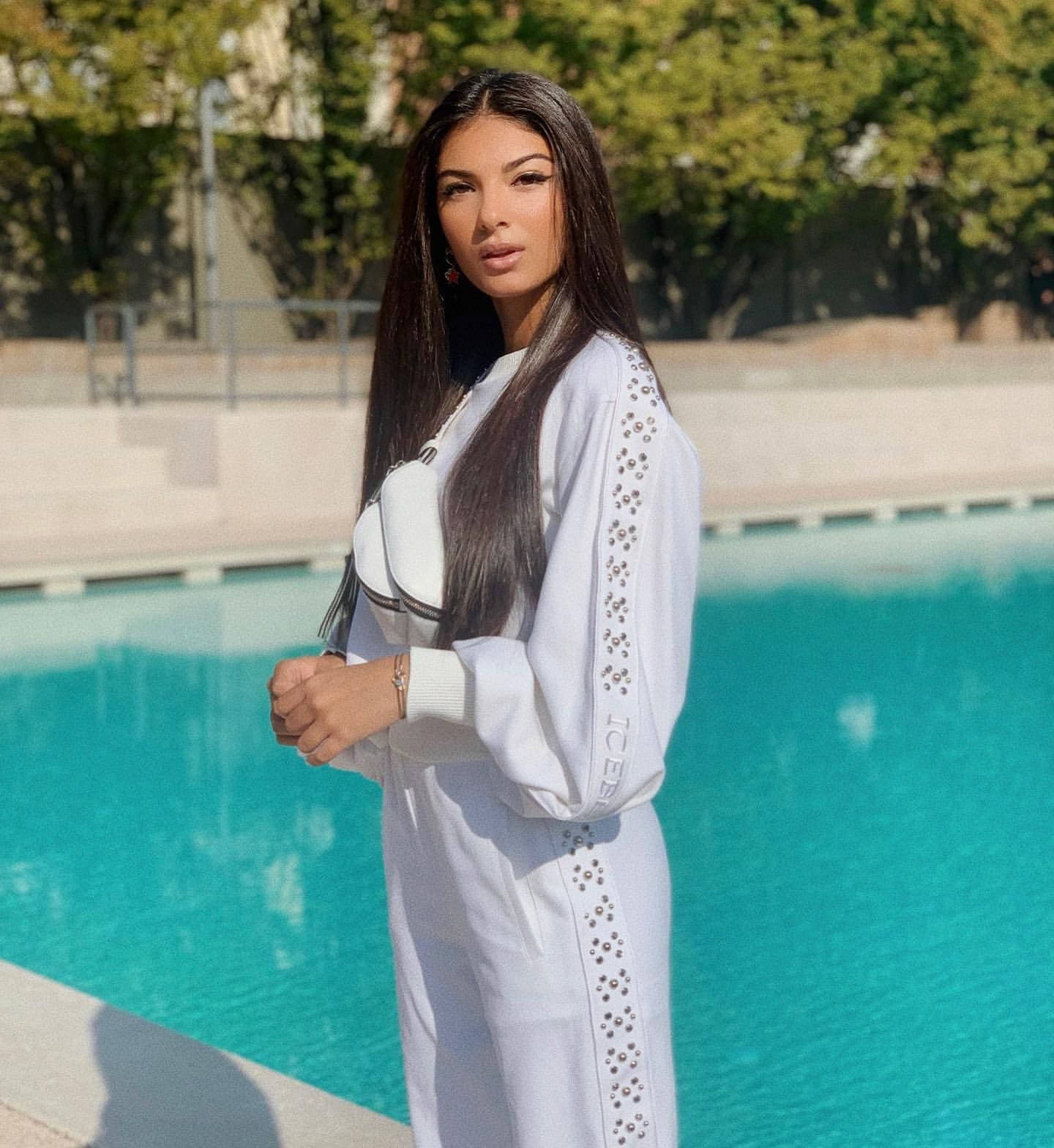 Beautiful Woman 桌布 壁紙 — 一位身穿白色刺繡運動服的女士在明亮的陽光下自信地站在碧綠色的游泳池旁。