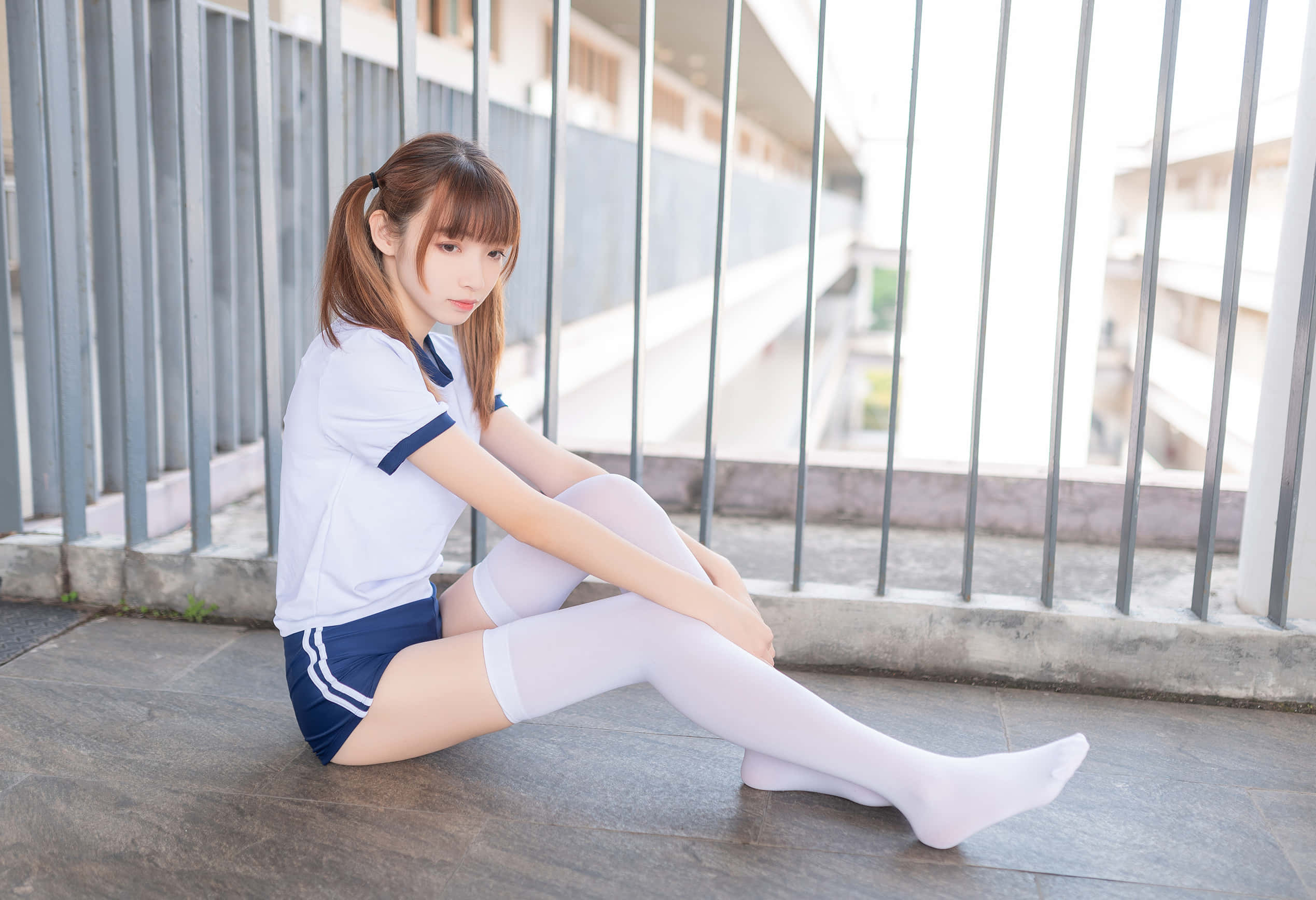 Cute Girl 桌布 壁紙 — 一位身穿白色和深藍色校服的年輕女性盤腿坐在瓷磚陽台地板上，若有所思地凝視著相機。