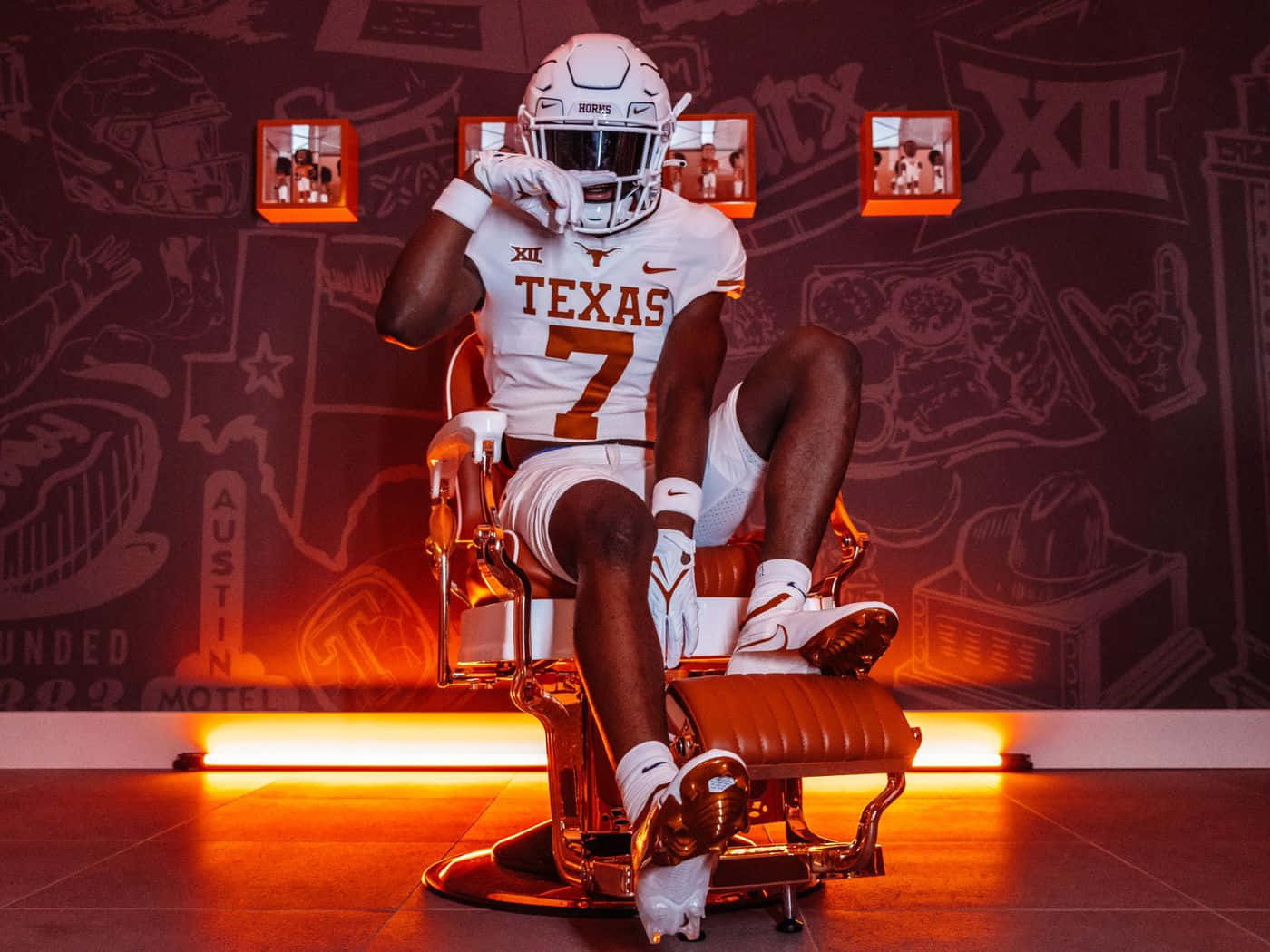 Texas Football 桌布 壁紙 — 一位身穿白色和焦橙色裝備的德州足球員，在溫暖的橙色燈光下自信地坐在復古理髮椅上。