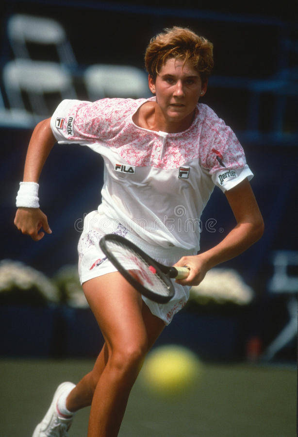 Monica Seles 桌布 壁紙 — 一位身穿白色和粉紅色運動裝備的女網球選手在綠色球場上向前撲出，用球拍擊打一個黃色網球。