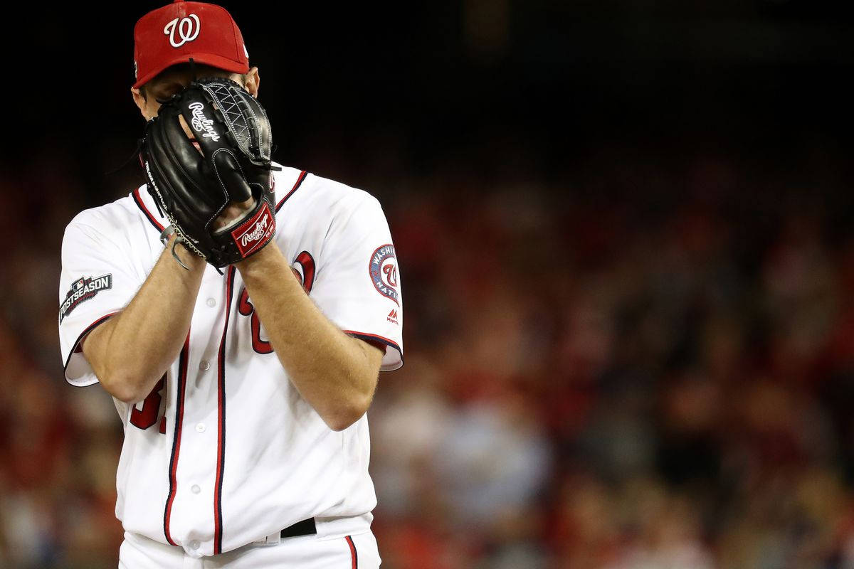 Max Scherzer 桌布 壁紙 — 一位身穿白色和紅色球衣的棒球投手在夜間球場用手套遮住臉。