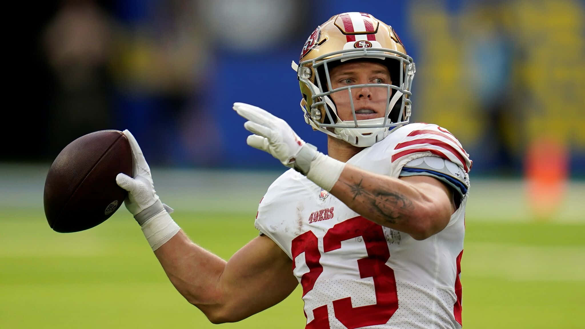 Christian Mccaffrey 桌布 壁紙 — 一位身穿白色和紅色球衣的舊金山四九人四分衛在綠色球場上專注地擲出橄欖球。