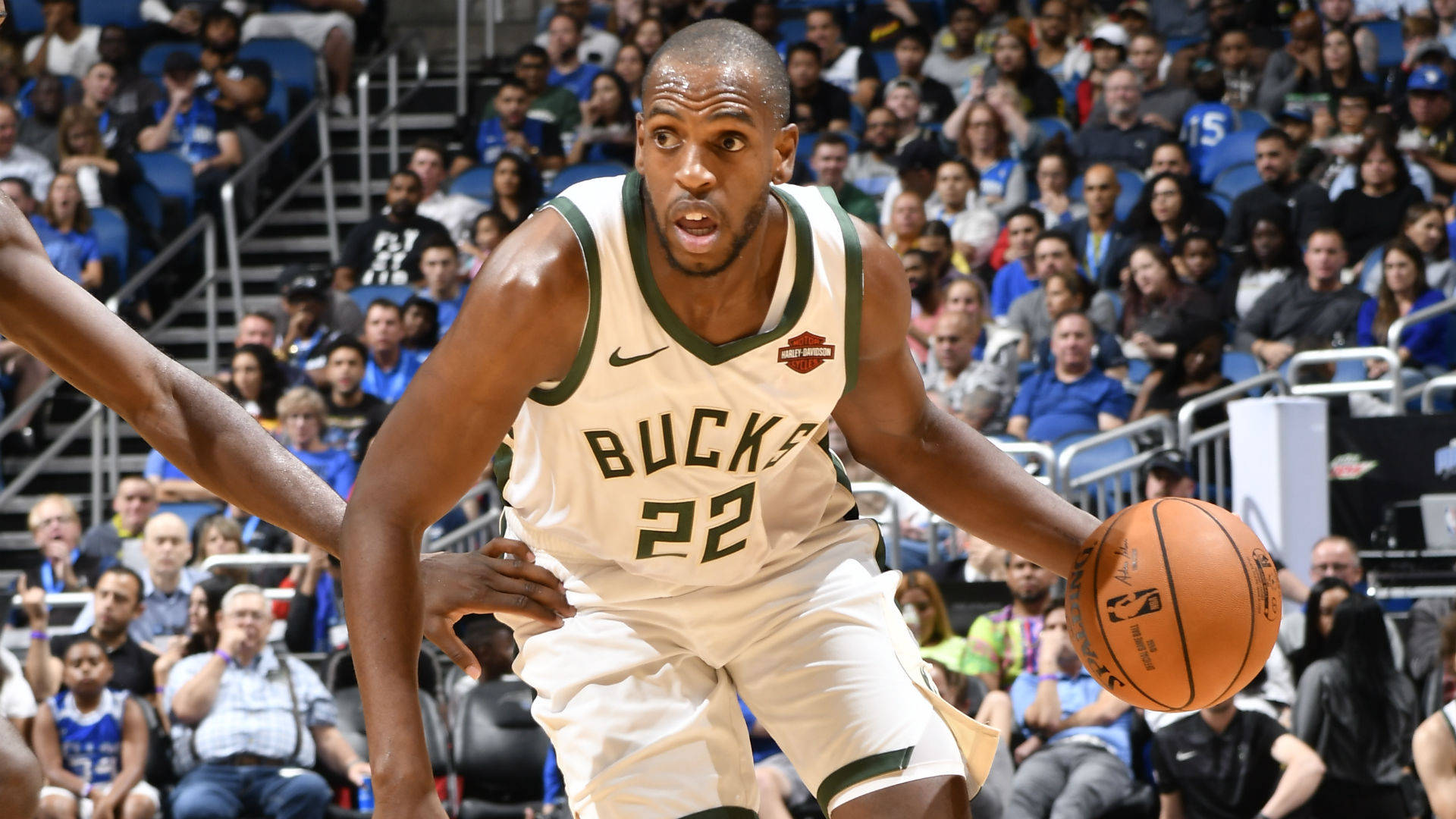 Khris Middleton 桌布 壁紙 — 一位身穿白色和綠色球衣的密爾瓦基公鹿籃球運動員在擠滿觀眾的場館中運球，同時被防守。