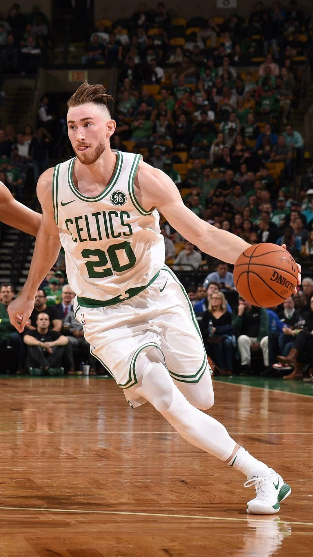 gordon hayward 桌布 壁紙 — 一位身穿白色和綠色球衣的波士頓塞爾提克籃球運動員在明亮的場館燈光下，專注地運球比賽。