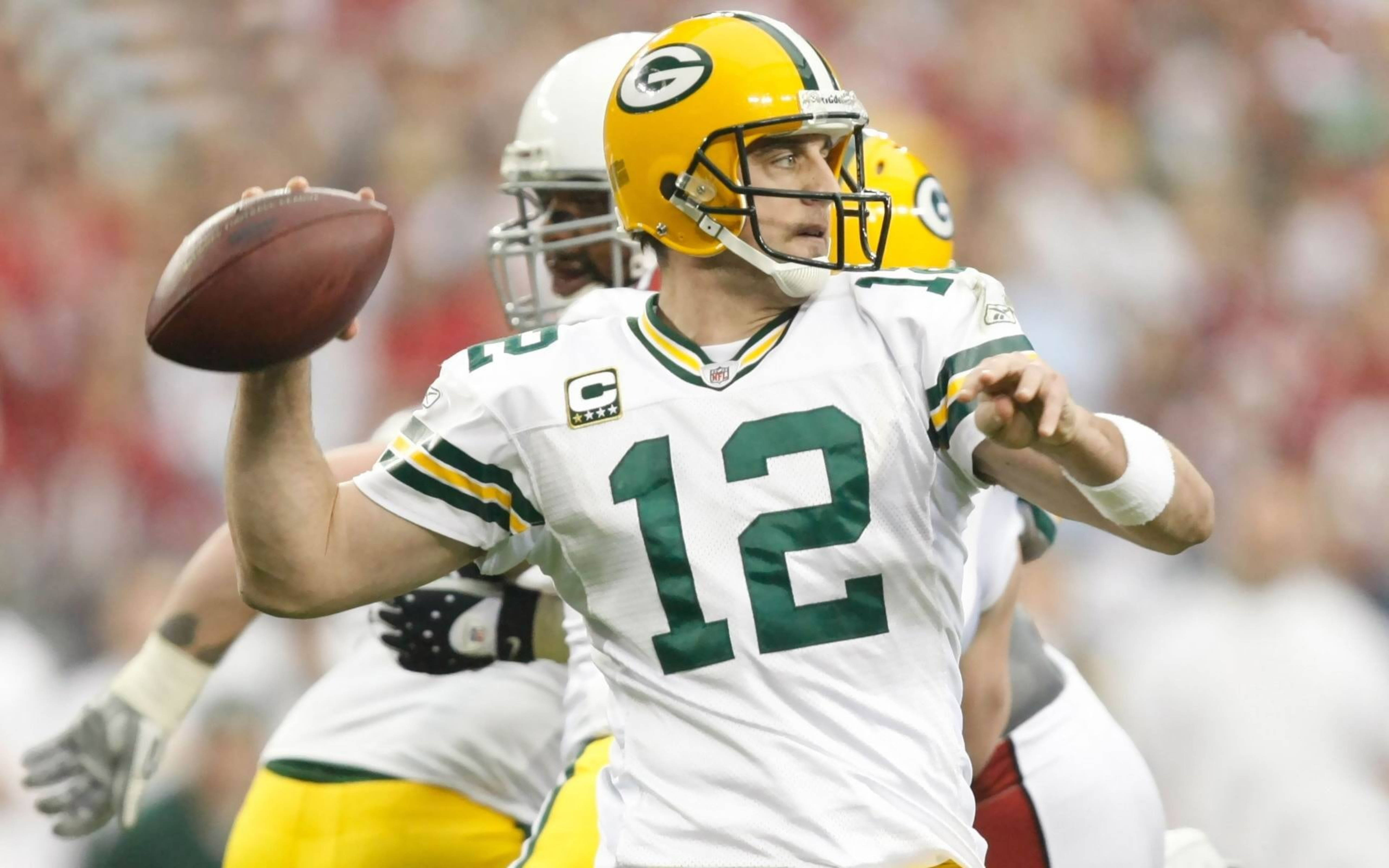 Aaron Rodgers 桌布 壁紙 — 一位身穿白色和綠色球衣的綠灣包裝工四分衛在白天比賽中投擲橄欖球，背景是模糊的體育場人群。