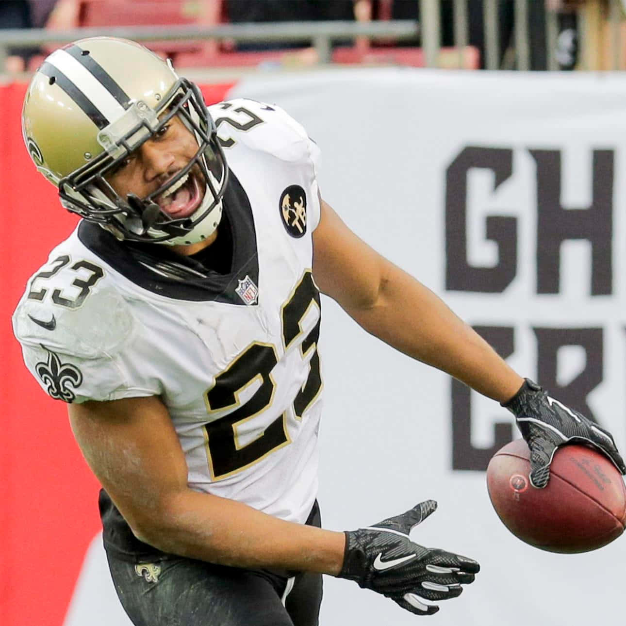 New Orleans Saints 桌布 壁紙 — 一位身穿白色和金色球衣的紐奧良聖徒隊美式足球員在比賽中拿著紅色足球慶祝。