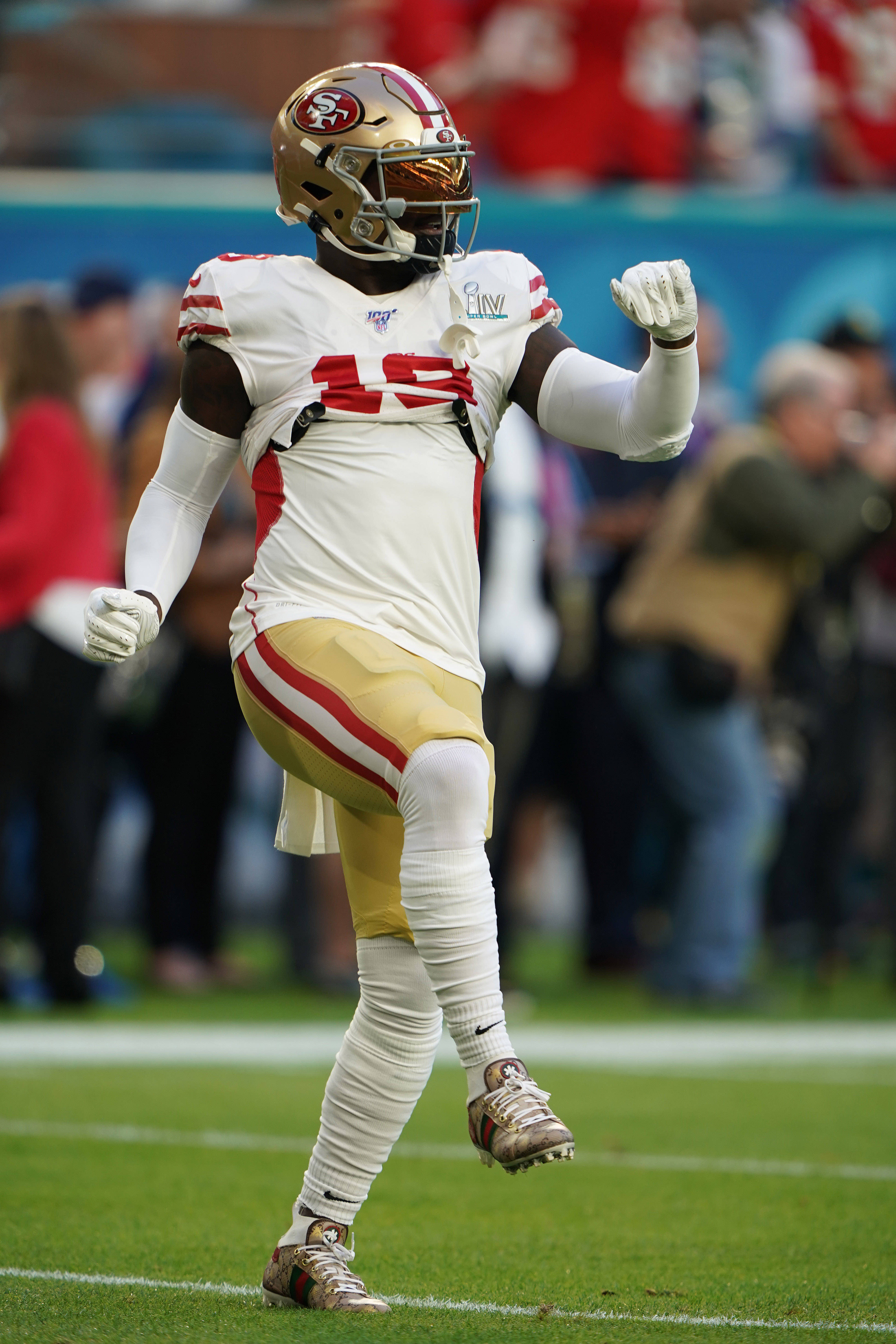 Deebo 桌布 壁紙 — 一位身穿白色和金色球衣的舊金山49人美式足球員在綠色球場上慶祝，背景是模糊的體育場人群。