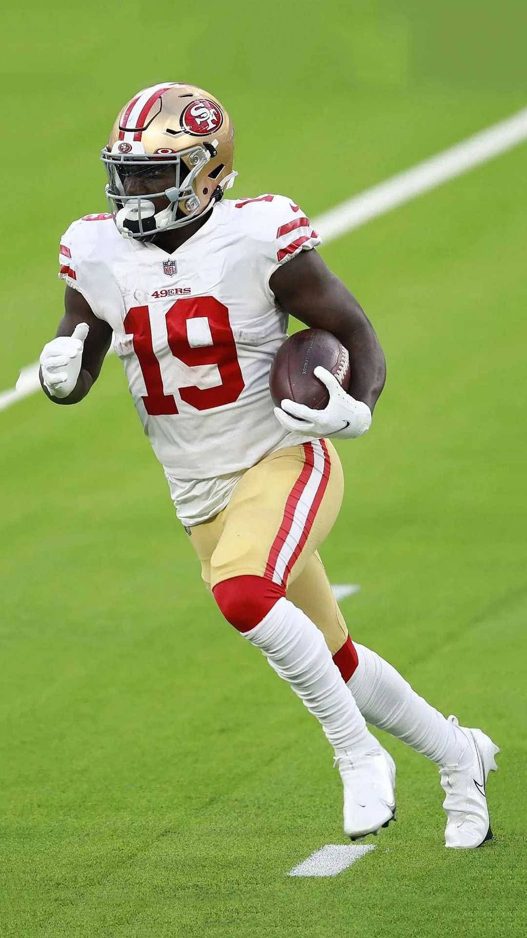 Deebo 桌布 壁紙 — 一位身穿白色和金色球衣的舊金山四九人美式足球員，在充滿活力的綠色球場上帶球衝刺。