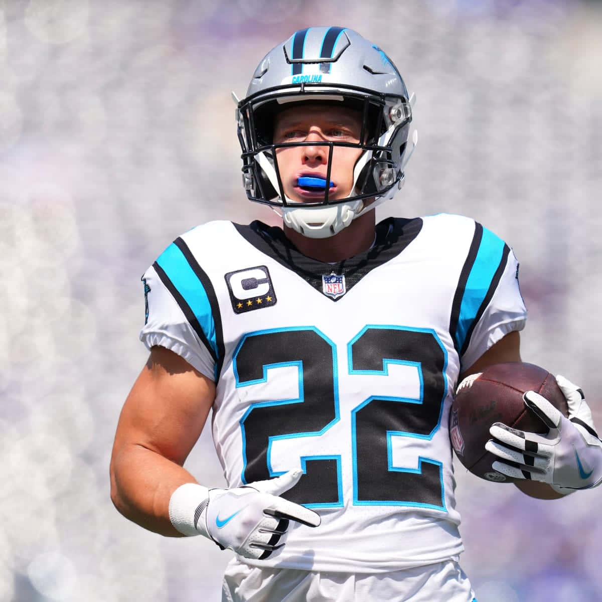 Christian Mccaffrey 桌布 壁紙 — 一位身穿白色和青綠色球衣的卡羅萊納黑豹隊美式足球員，在明亮的日光下抱著足球向前看。