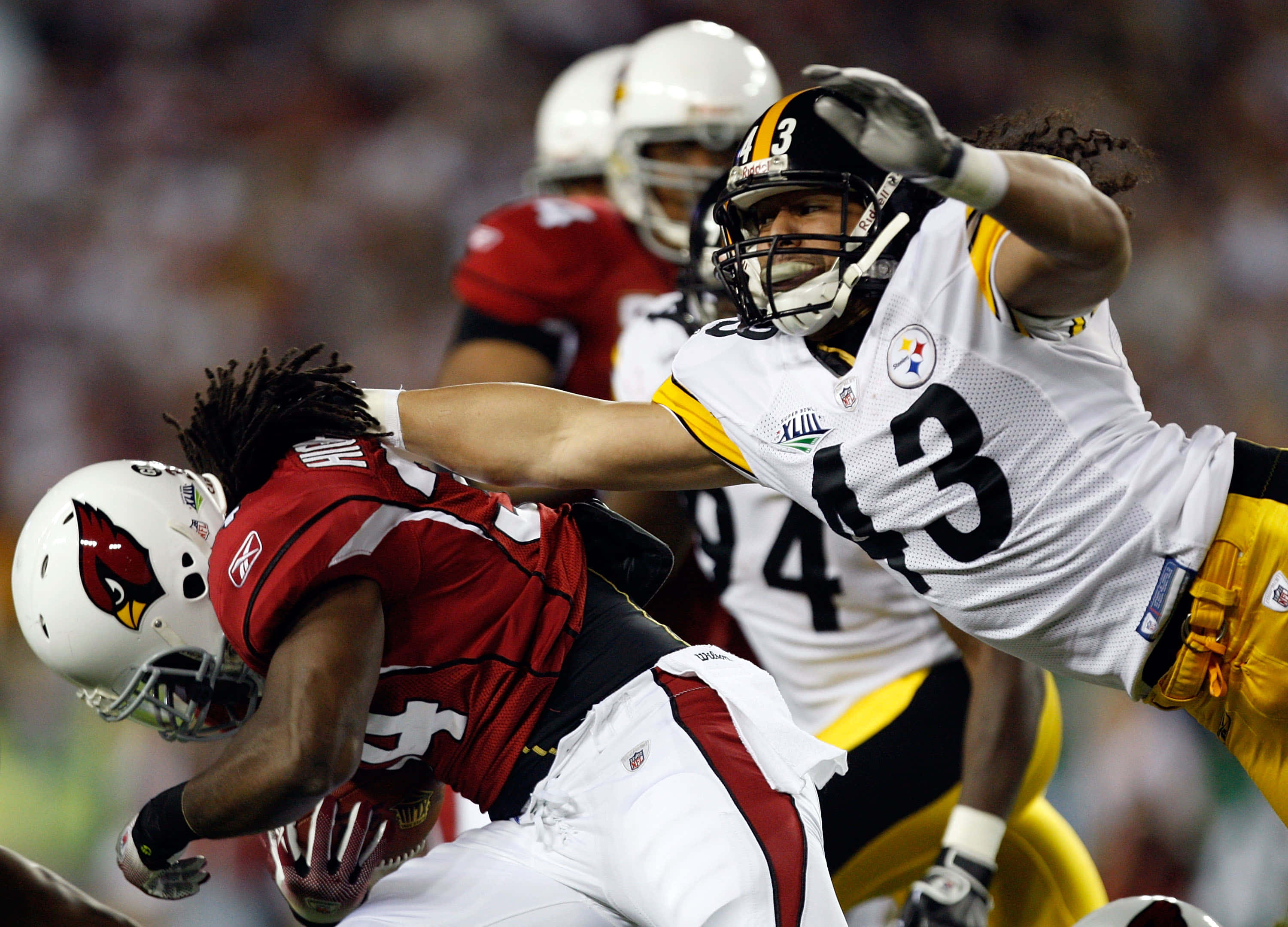 Troy Polamalu 桌布 壁紙 — 一位身穿白色和黃色球衣的匹茲堡鋼人隊球員在夜間美式足球比賽中飛身擒抱一位身穿紅色的亞利桑那紅雀隊球員。