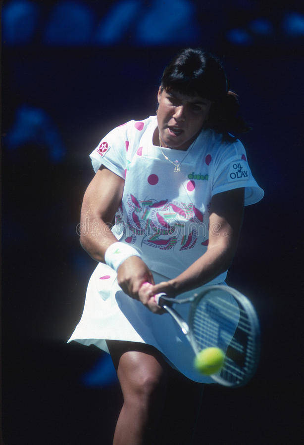 Jennifer Capriati 桌布 壁紙 — 一位身穿白色圓點裙的女網球選手在明亮的體育場燈光下揮拍擊打黃色網球。