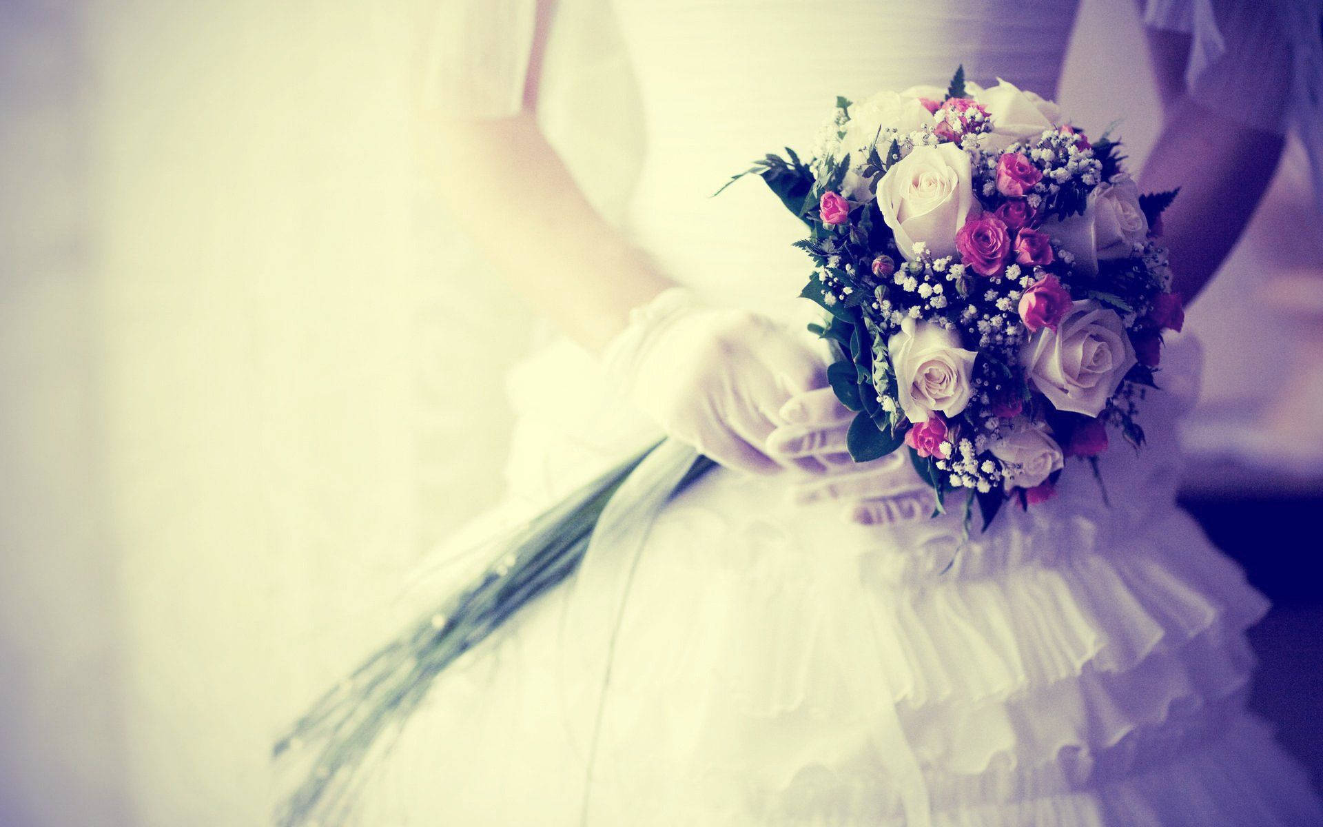 Wedding 桌布 壁紙 — 一位身穿白色婚紗和手套的新娘，在柔和模糊的背景前，手持一束粉紅和白色玫瑰，搭配綠葉。