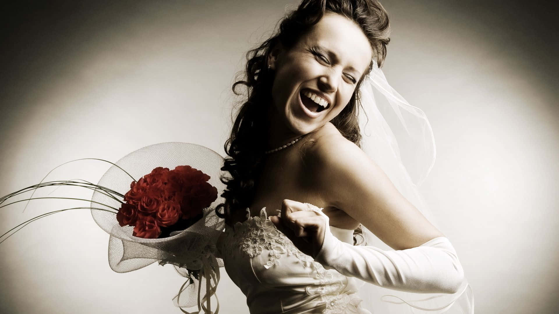 Bridal 桌布 壁紙 — 一位身穿白色婚紗的快樂新娘，在柔和的灰色背景前，捧著一束紅玫瑰開懷大笑。