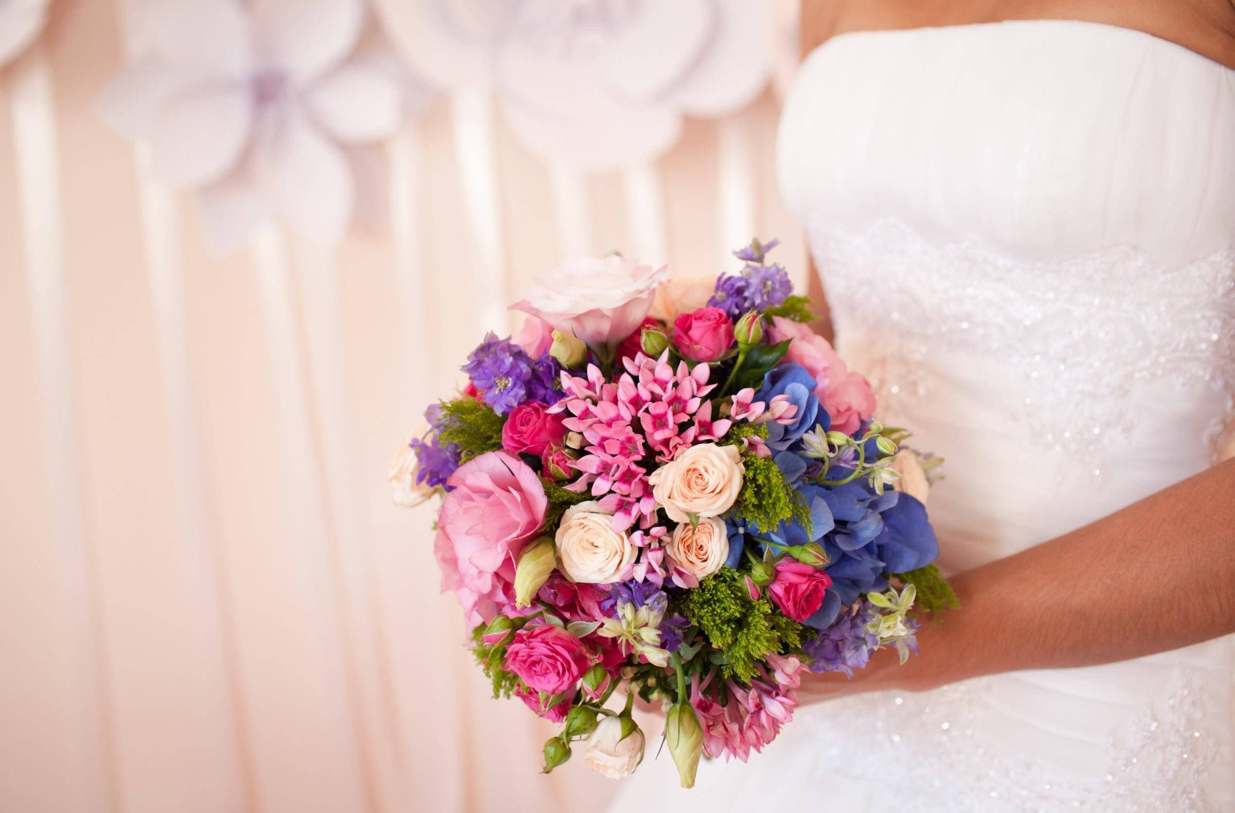 Bride 桌布 壁紙 — 一位身穿白色婚紗的新娘，在柔和的粉紅色背景下，手持一束鮮豔的粉、藍、紫色花束。