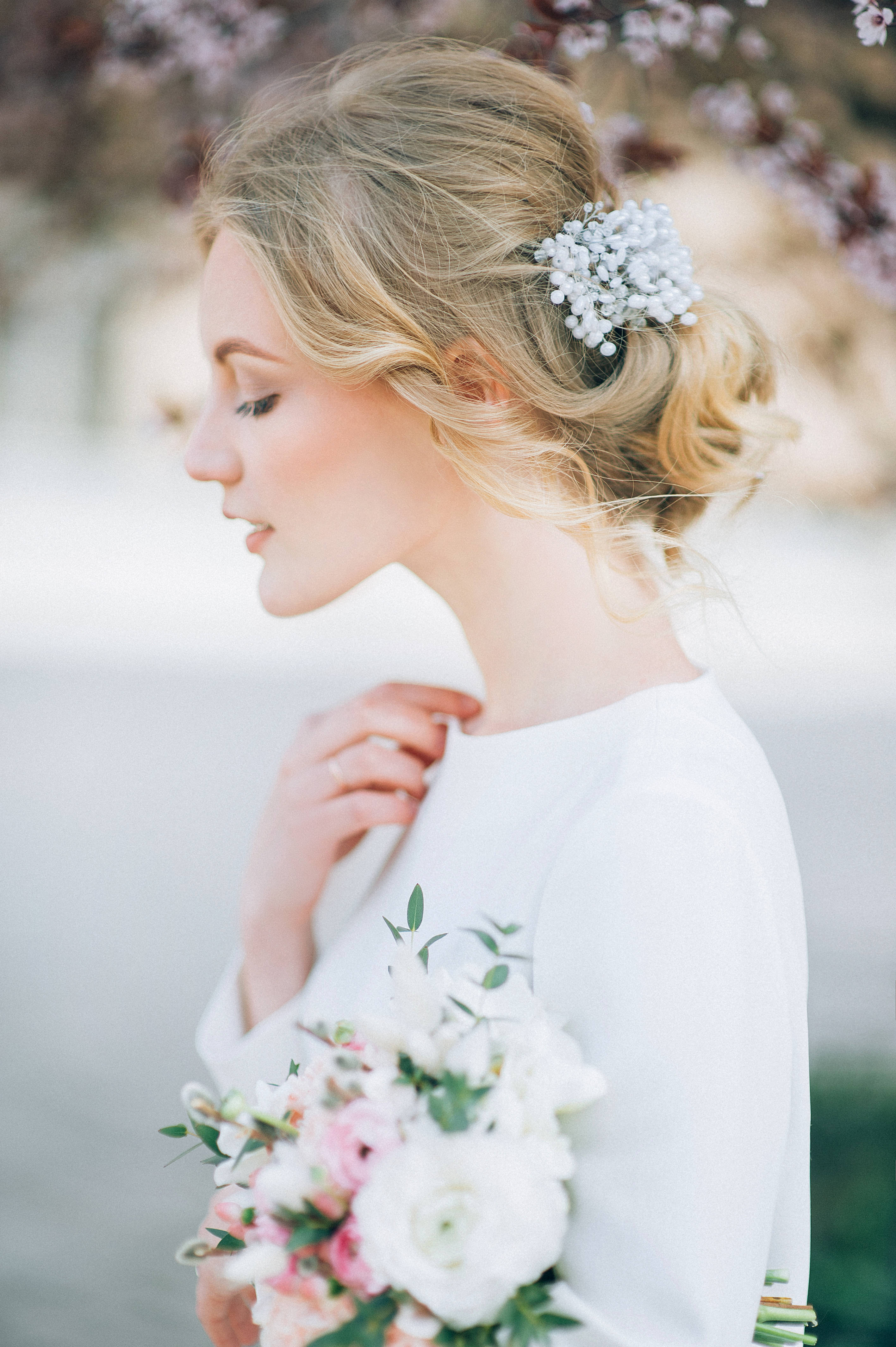 Wedding Aesthetic 桌布 壁紙 — 一位身穿白色婚紗的新娘在柔和春光下手持花束，背景是盛開的樹木。