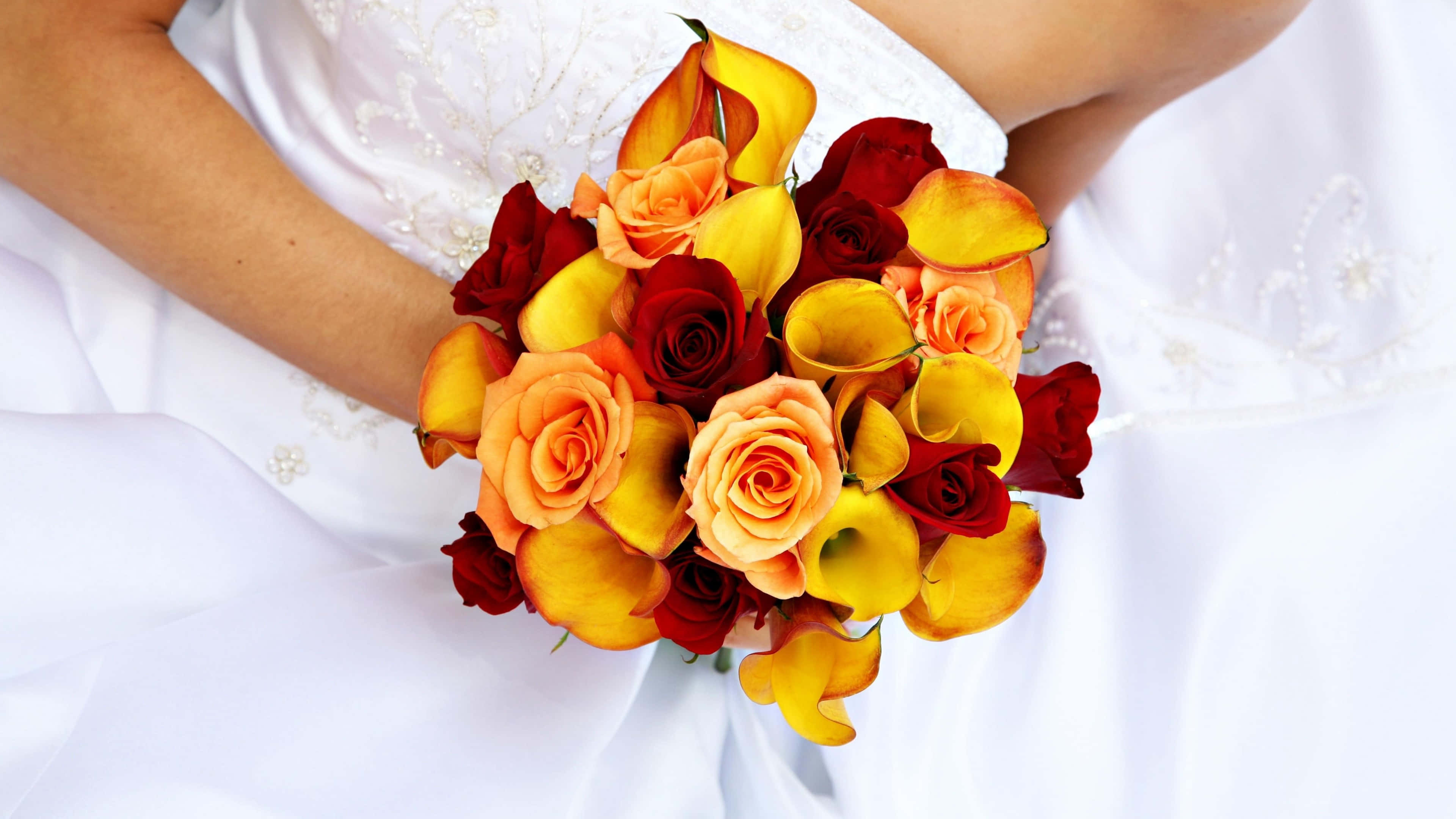 Wedding Bouquet 桌布 壁紙 — 一位身穿白色婚紗的新娘懷抱一束由橙、黃、紅玫瑰和馬蹄蓮組成的鮮豔花束。
