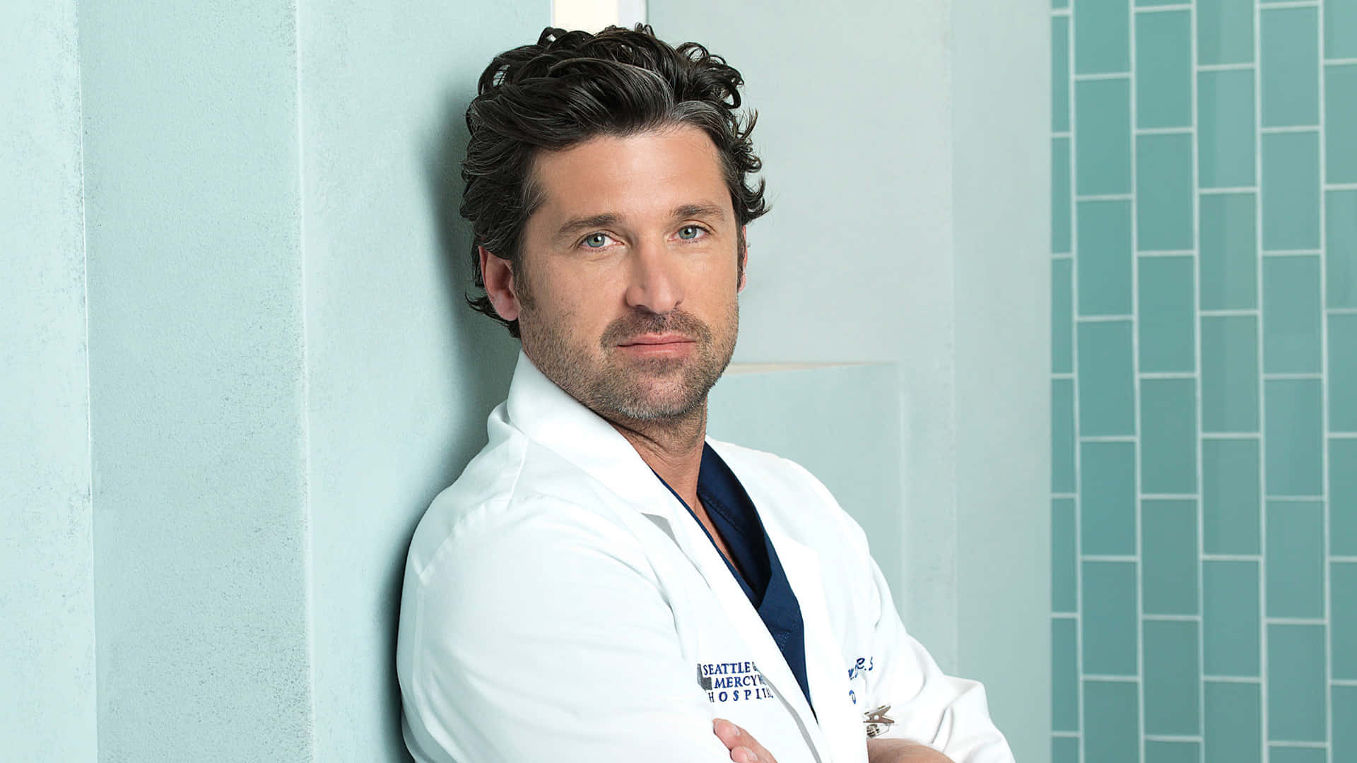 Grey's Anatomy 桌布 壁紙 — 一位身穿白色實驗室外套的男醫生，雙手交叉，靠在一面淺藍色瓷磚牆上。