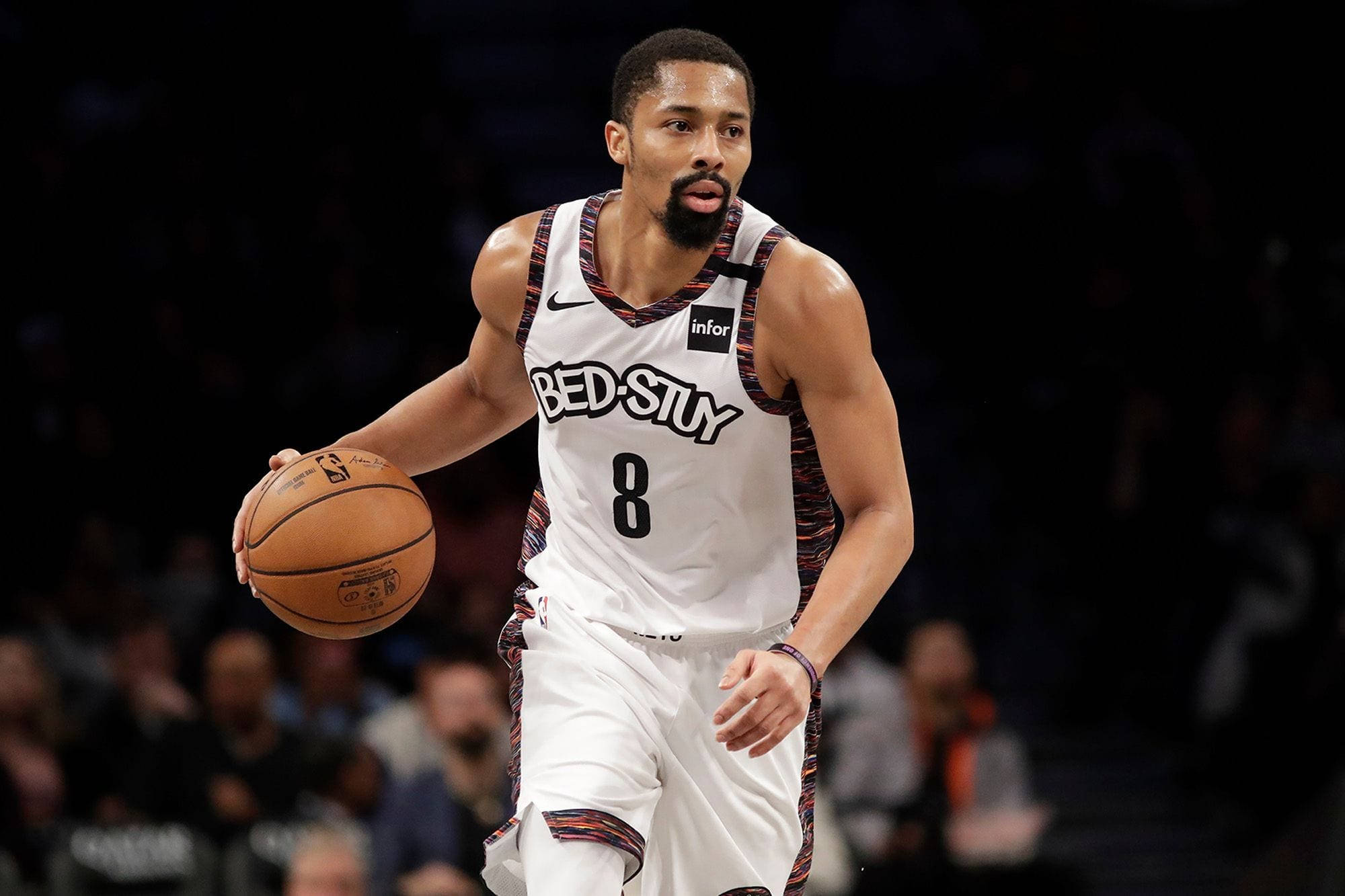 spencer dinwiddie 桌布 壁紙 — 一位身穿白色布魯克林球衣的籃球運動員在場館燈光下專注地運球。