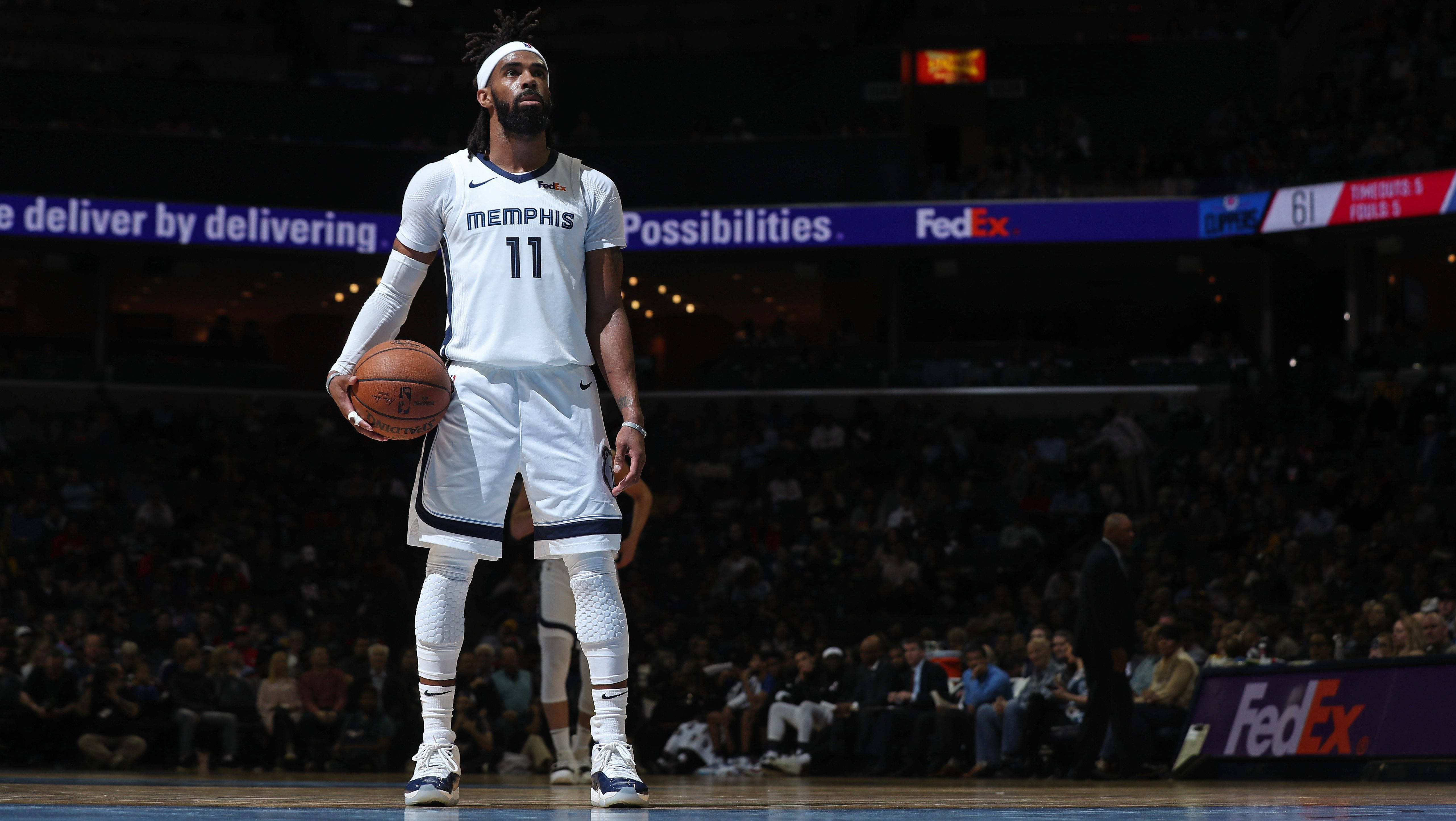 mike conley 桌布 壁紙 — 一位身穿白色曼菲斯球衣的籃球運動員在場館燈光下持球準備，球迷們在看台上觀看。