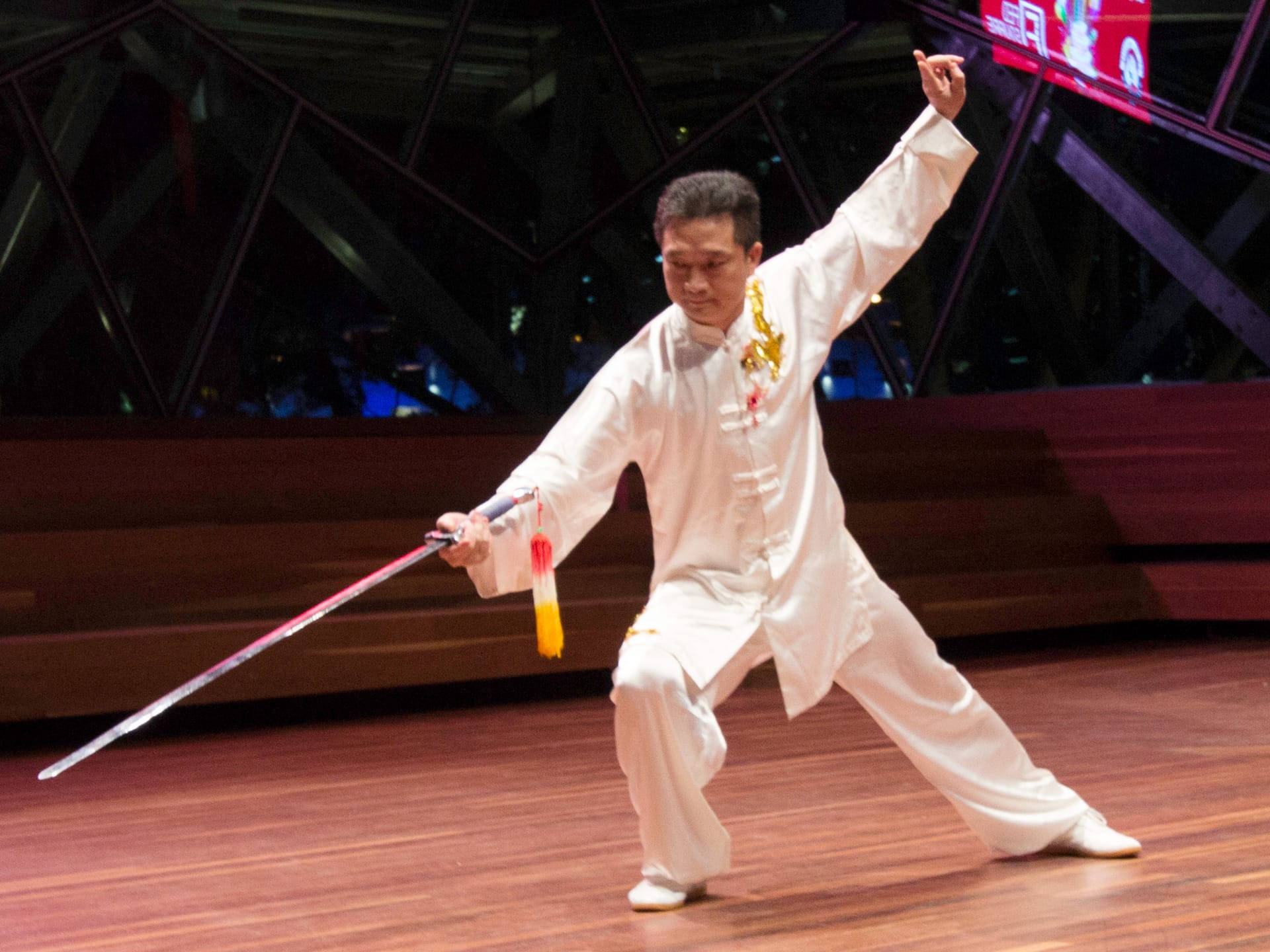 martial arts 桌布 壁紙 — 一位身穿白色服裝的武術家在幾何燈光下的木製舞台上表演精準的劍術招式。