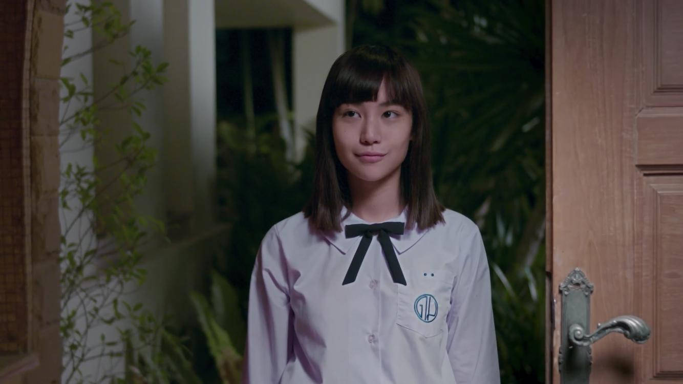 高清 桌布 壁紙 — 一位身穿白色校服、繫著黑色蝴蝶結的年輕女子，站在光線昏暗的門口，周圍環繞著綠植和木門。